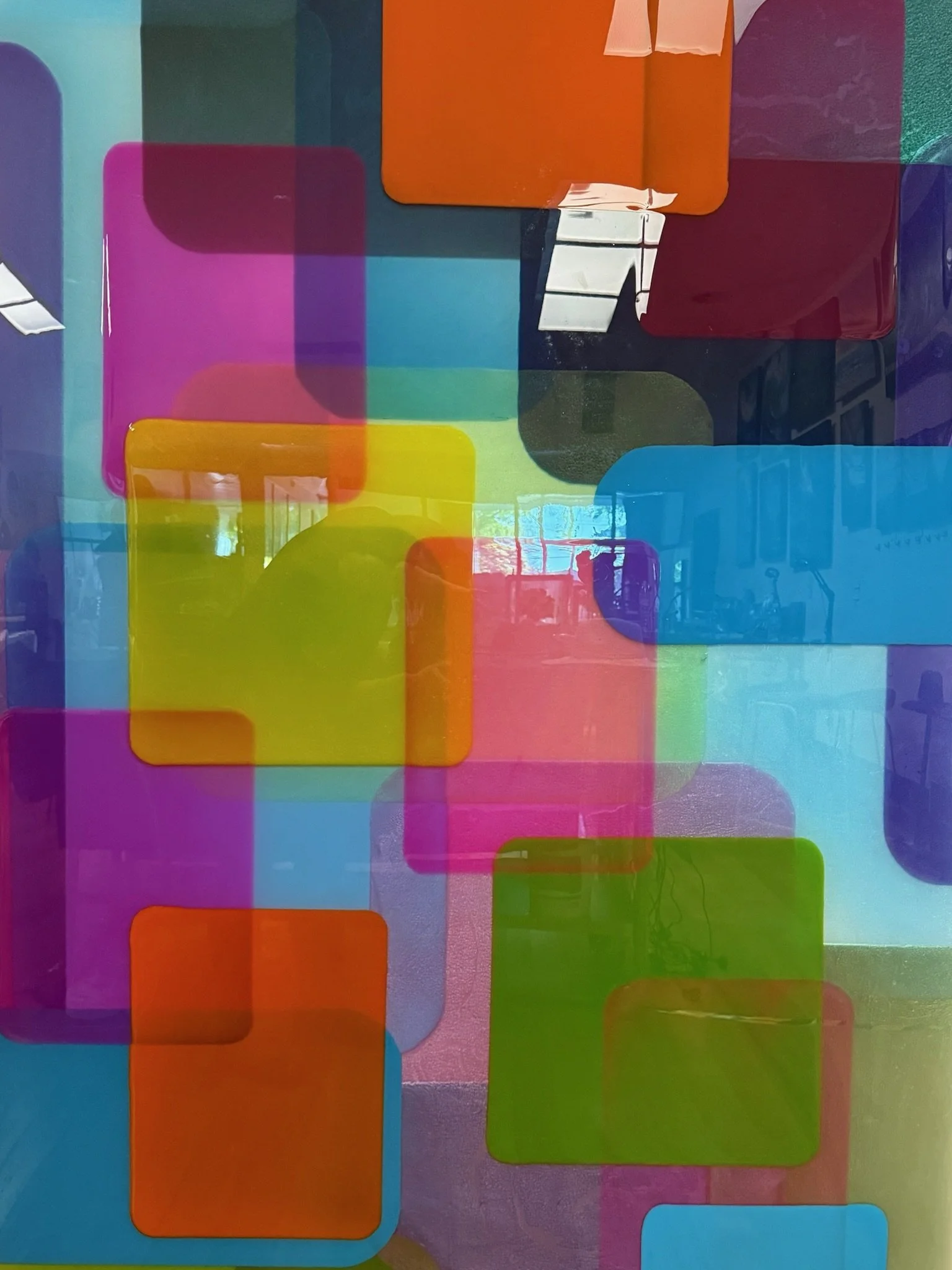 Colorful glass panels arranged in different shapes and colors, including purple, pink, orange, green, blue, red, and yellow, with some reflections and a window in the background.