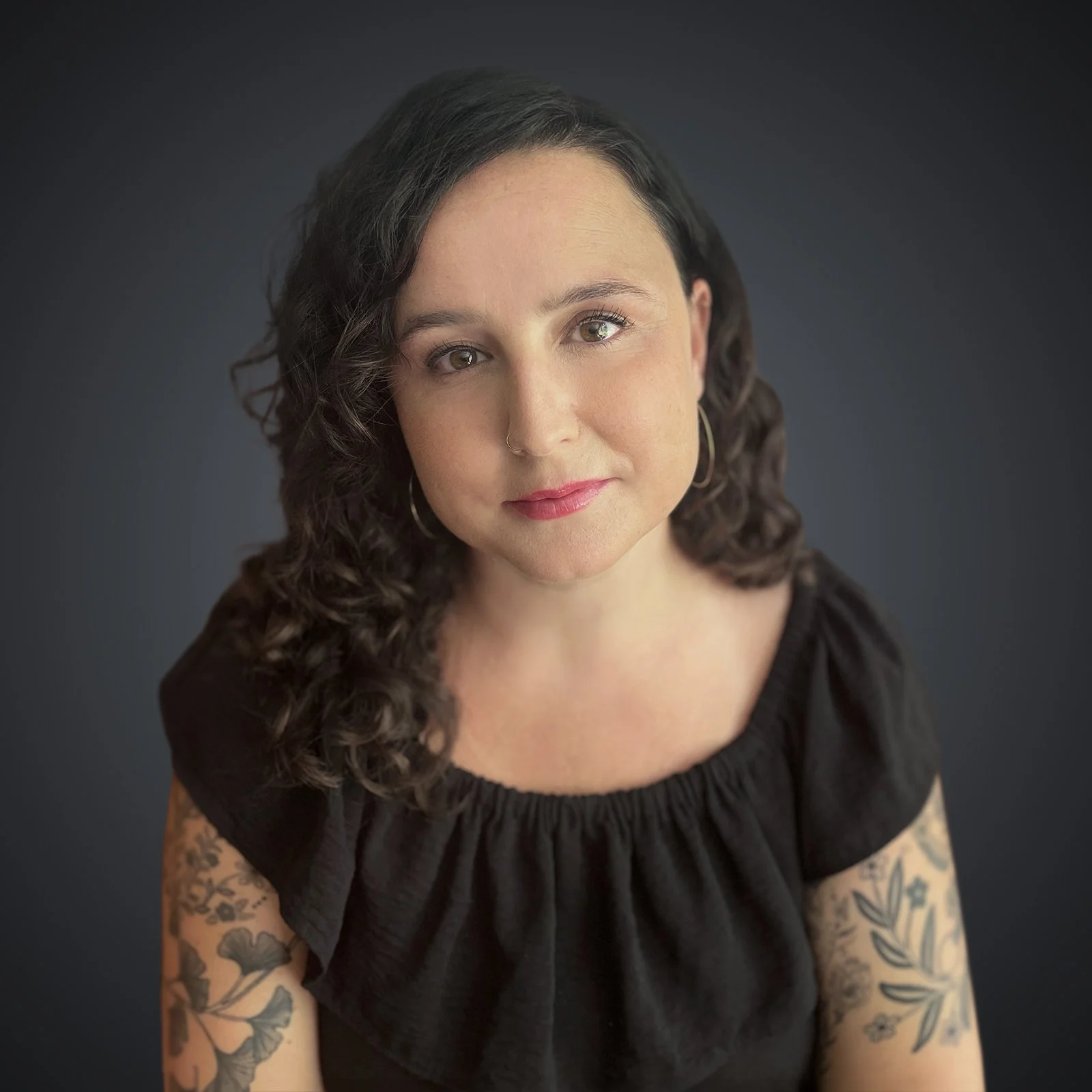 Portrait of Selene Altamirano-Farrell, LCSW, a New York therapist with dark, curly hair, wearing a black top with floral tattoos visible.