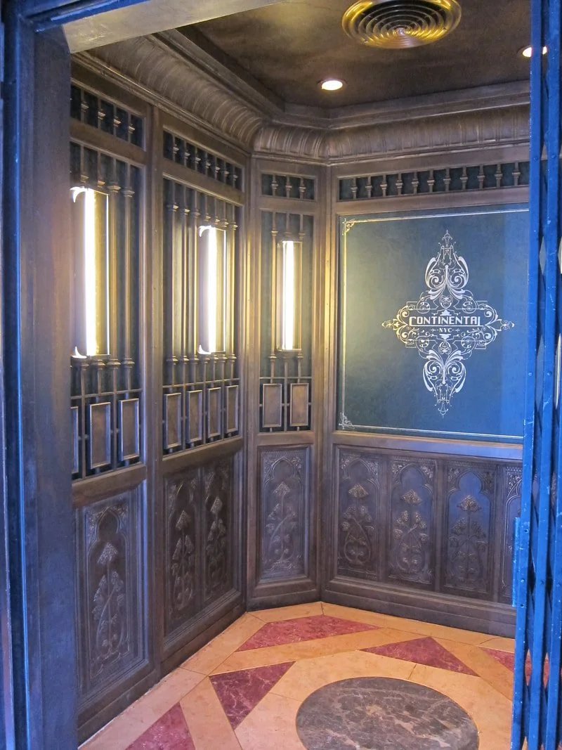 An ornate wooden corner wall with decorative paneling and vertical light fixtures, featuring a dark green sign with the word 'Continental' and intricate designs.