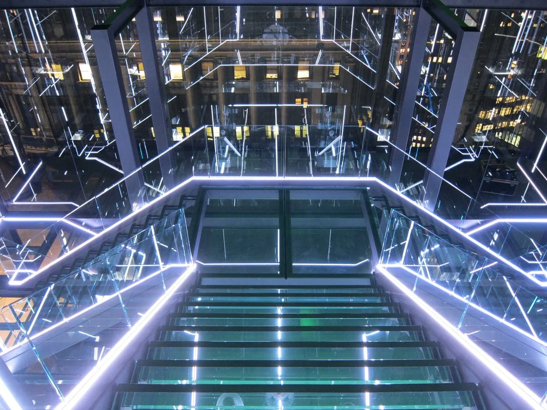 Futuristic glass staircase with illuminated LED lights and mirrored walls in a modern building.