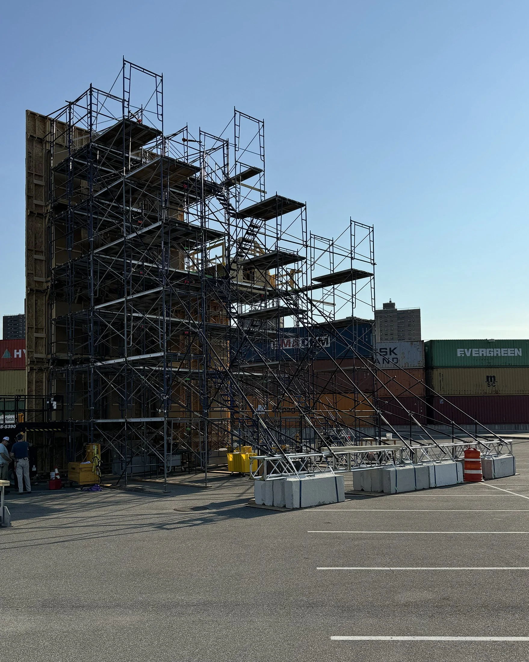 Construction scaffolding set up in a parking lot with shipping containers in the background and a clear blue sky.