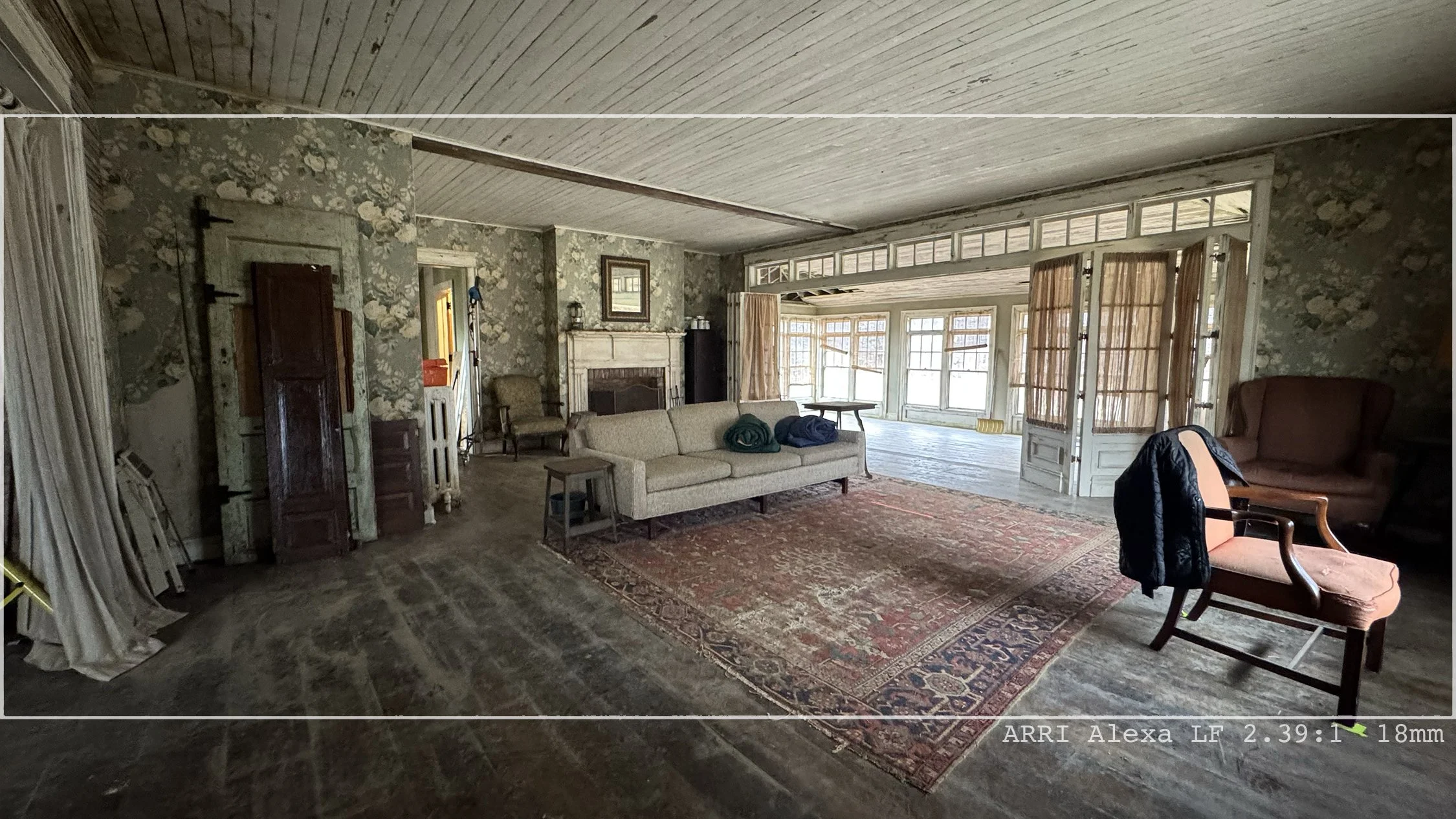 Living room with floral wallpaper, fireplace, large windowed sunroom, vintage furniture, and a rug.