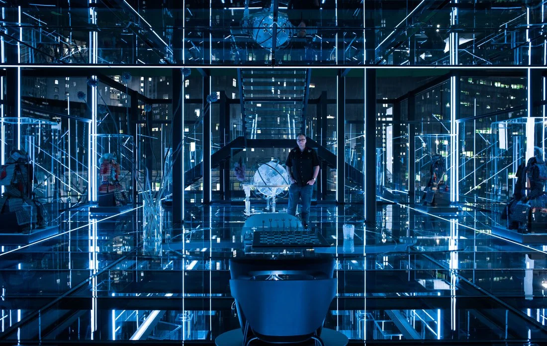 A person standing in a high-tech, mirrored room with blue lighting, illuminated lines, and futuristic design elements.