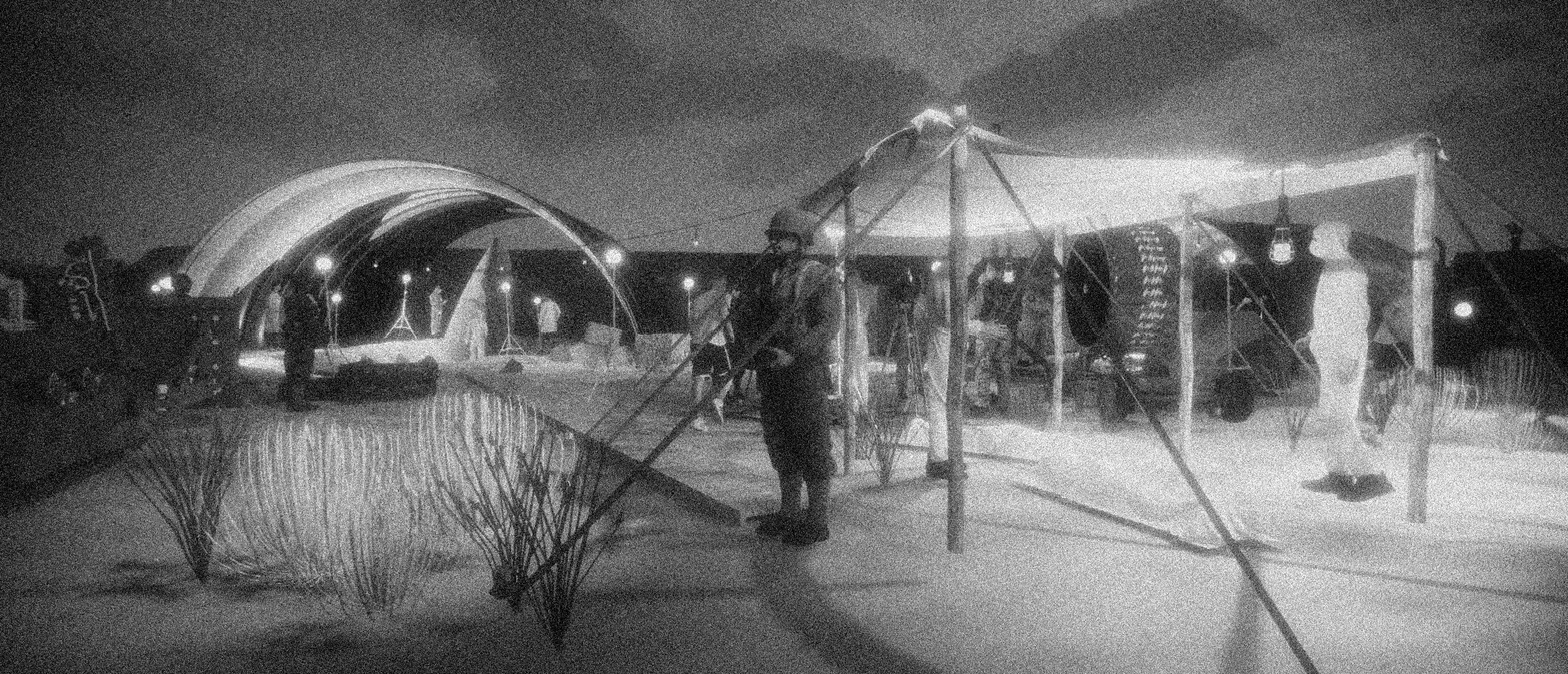 Nighttime scene with a playground or amusement park area under dim lighting, featuring a swing set and a dome-shaped structure. Several people are present, some on bicycles, and there are decorative elements in the scene.