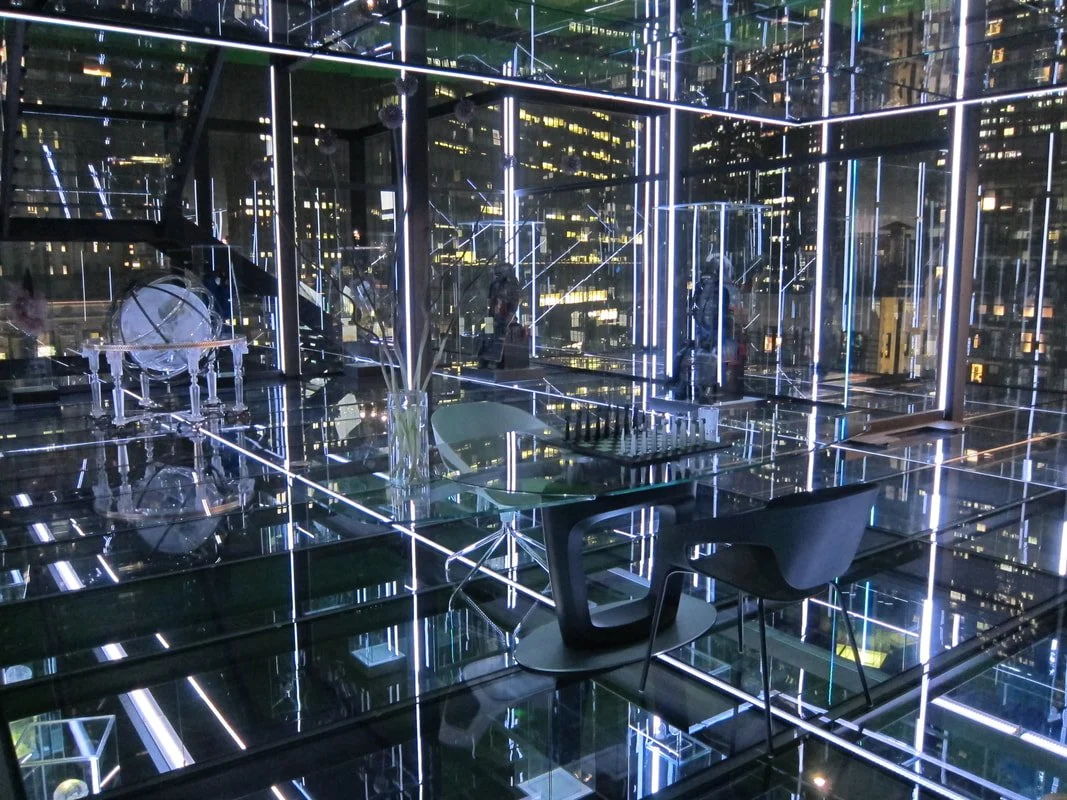 A modern, high-tech interior with glass walls, illuminated by neon lights, featuring furniture and musical instruments, overlooking a city skyline at night.