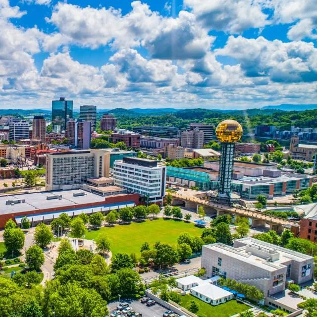 Cityscape with a prominent gold sphere observation tower, various modern buildings, green park, and partly cloudy sky.