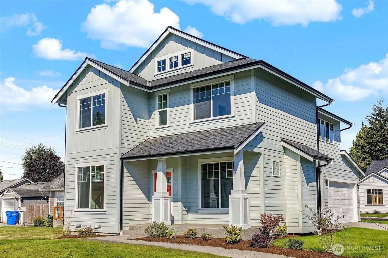 Front view of a modern multi-story house with light-colored siding, large windows, covered porch, and a one-car garage in a suburban neighborhood.