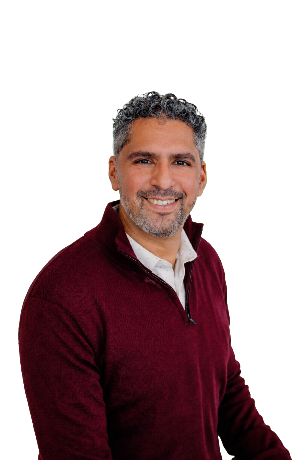 A smiling man with gray curly hair and a beard, wearing a burgundy zip-up sweater over a white collared shirt, against a black background.