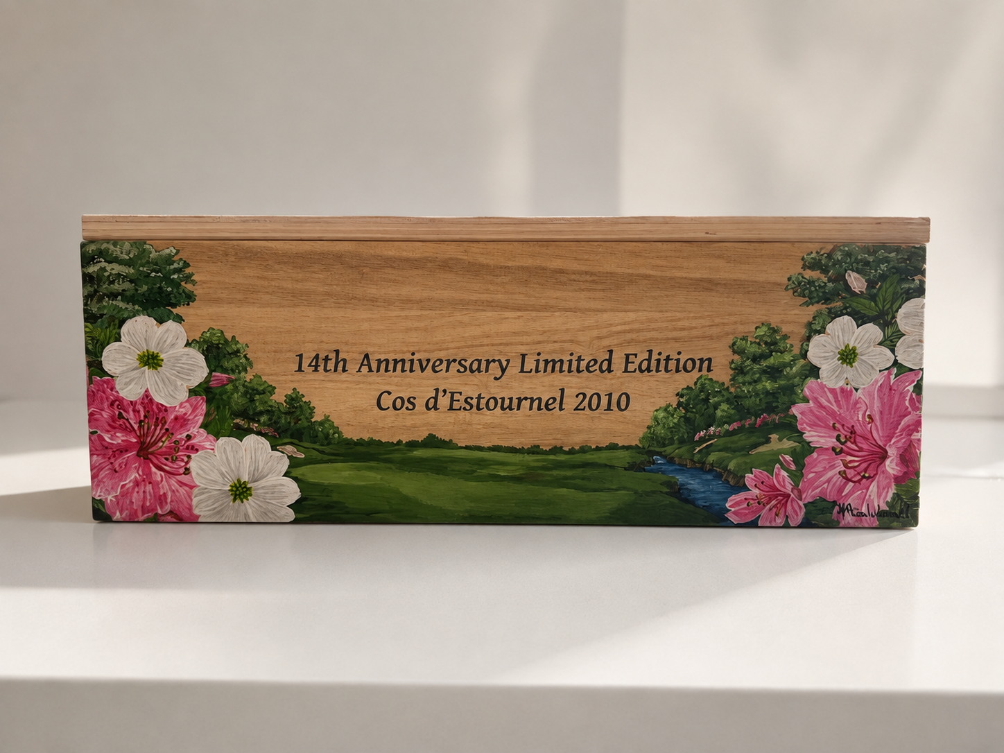 A wooden box with floral painting on the sides, displaying text that reads '14th Anniversary Limited Edition Cos d'Estournel 2010'.