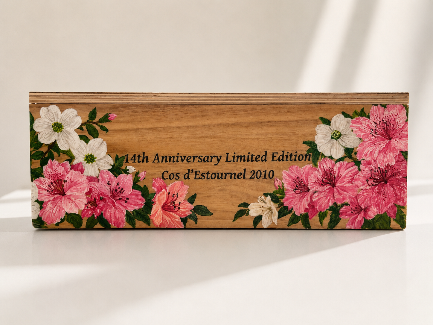 A wooden box decorated with pink and white flowers, containing the text '14th Anniversary Limited Edition Cos d’Estournel 2010'.