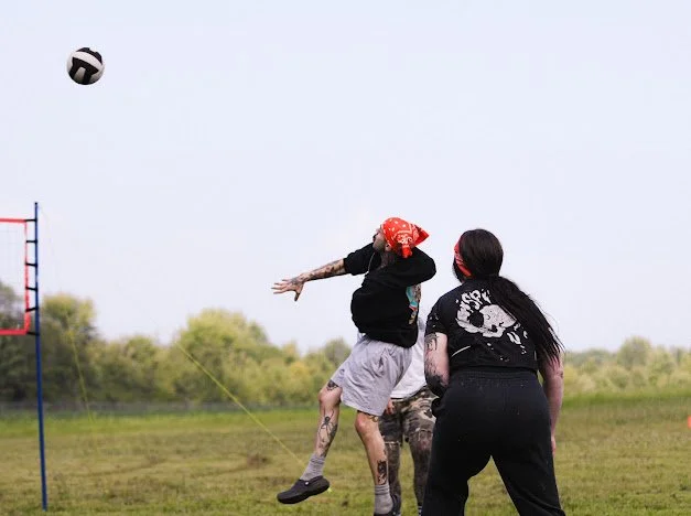 Two women and a child playing volleyball outdoors on grass field, with a volleyball in the air.