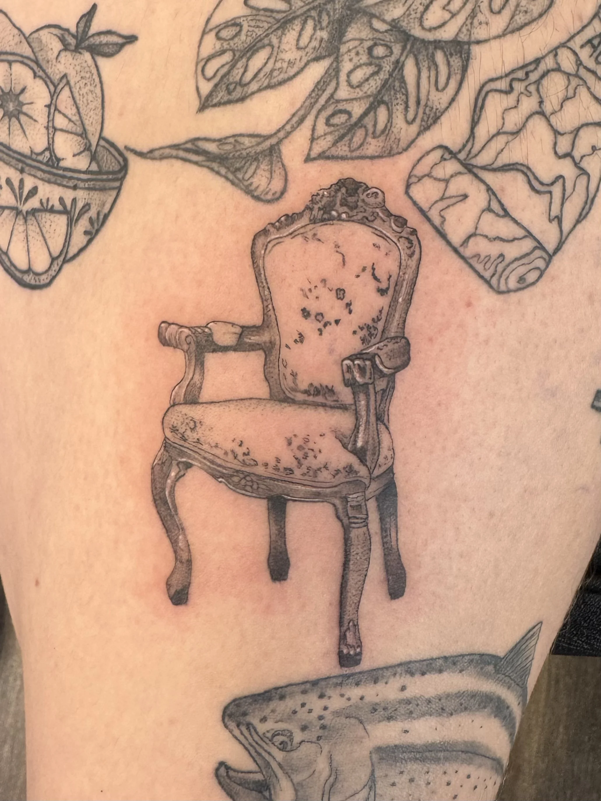 Tattoo of an armchair, a whale, a whale fin, a tiger, a fish, and a lemon in a bowl.