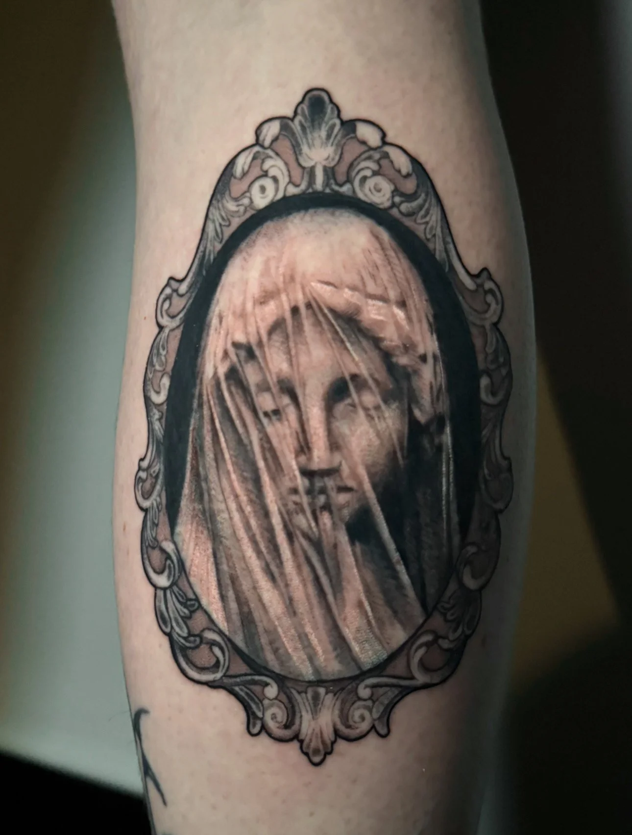 Tattoo of a Madonna-like woman with long hair, framed by an ornate, decorative border.