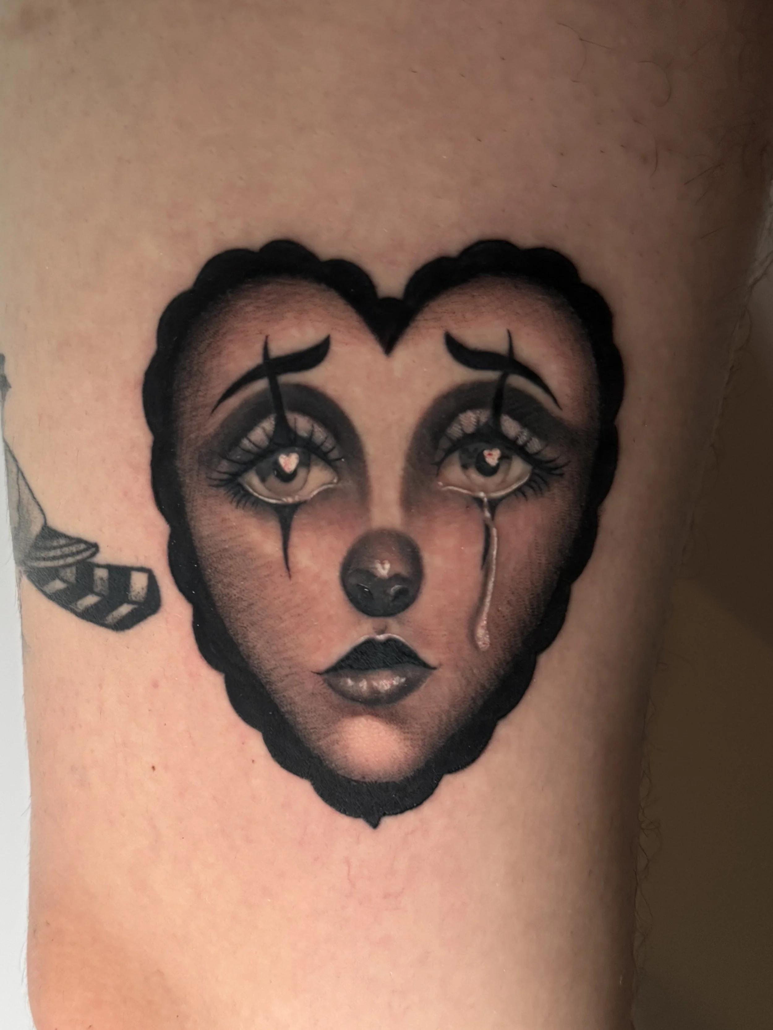 Tattoo of a female clown face with makeup, black outlines, and tears tattoo