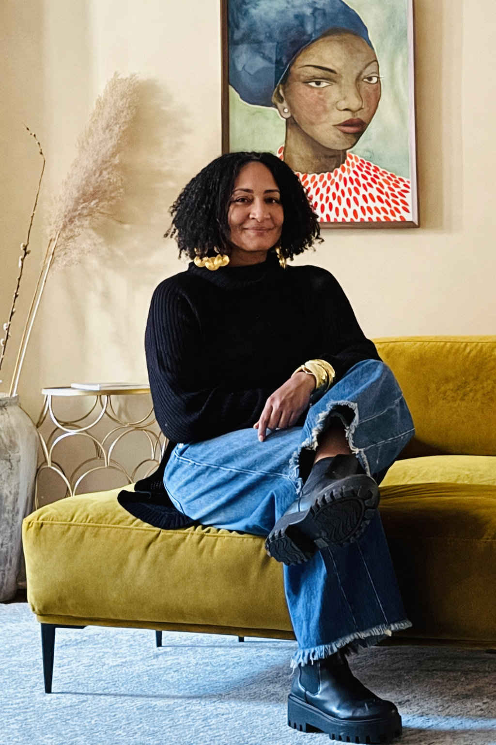 Nisha McNair seated on a mustard chair, wearing a black sweater and jeans