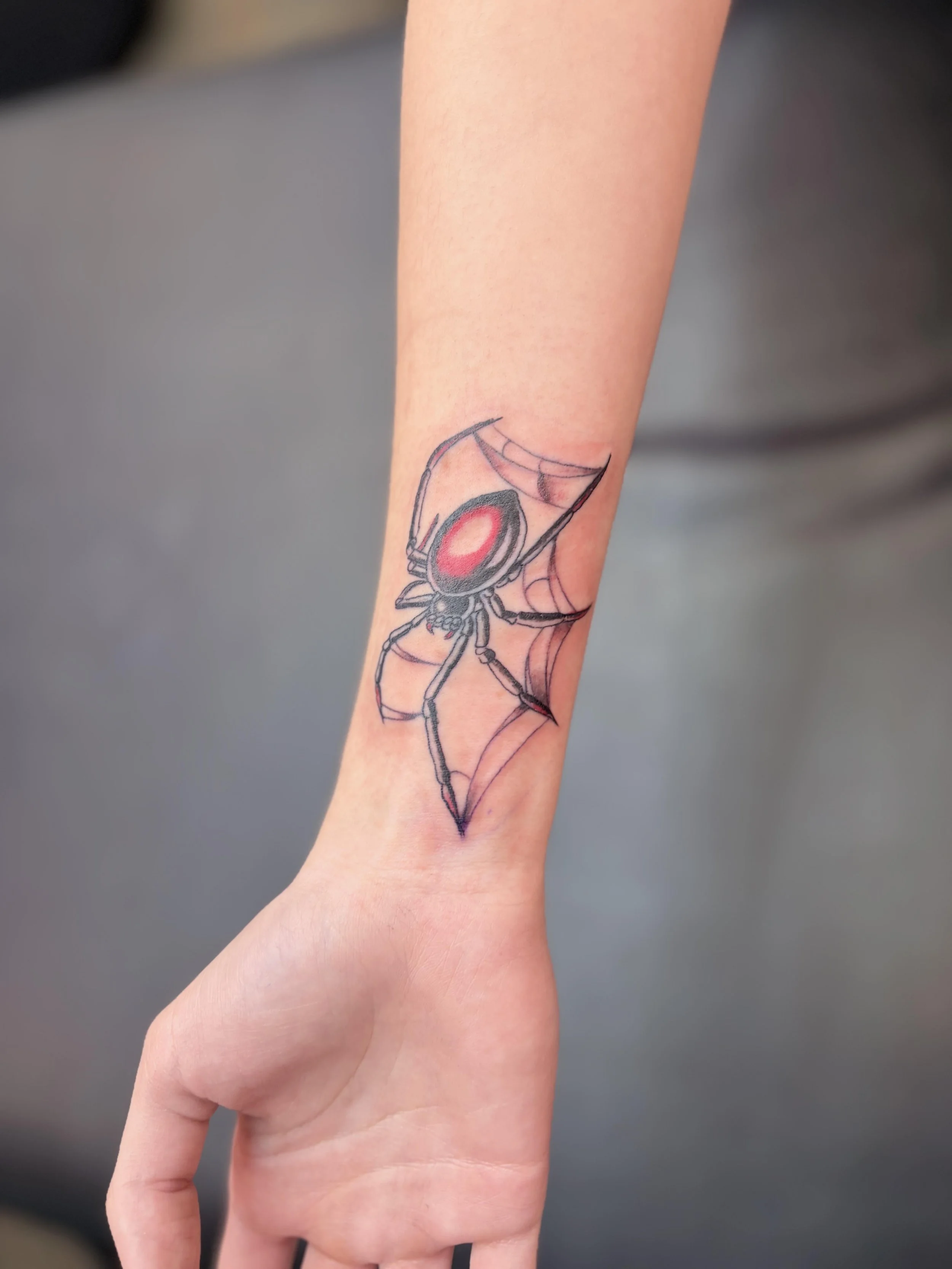 A person's forearm with a colorful spider web tattoo near the wrist.