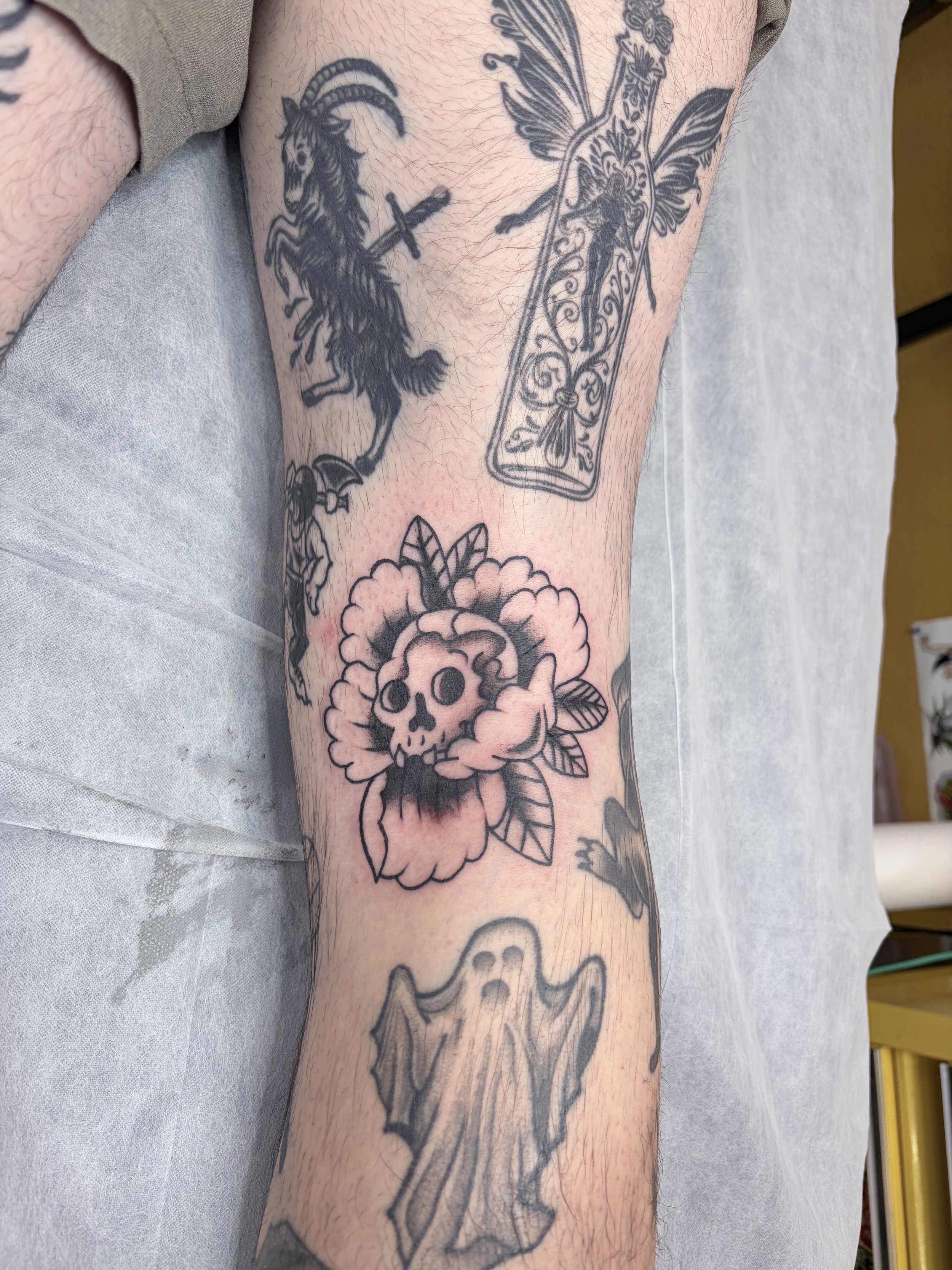 Tattoo of a goat with a cross and a steeple on its back, a butterfly, a skull with flowers, and a bat on a person's arm.