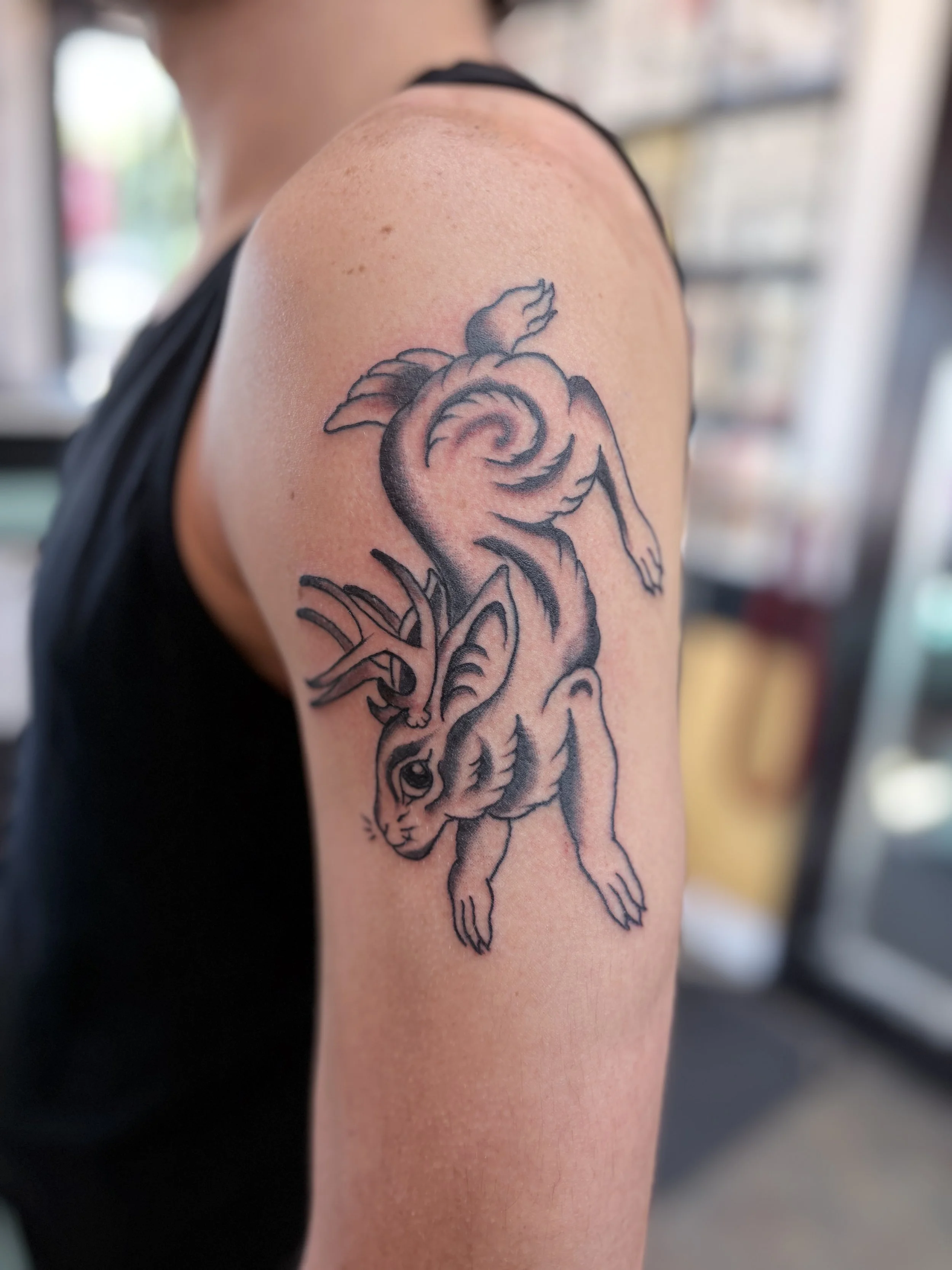 A black line tattoo of a jackalope on a person's upper arm.