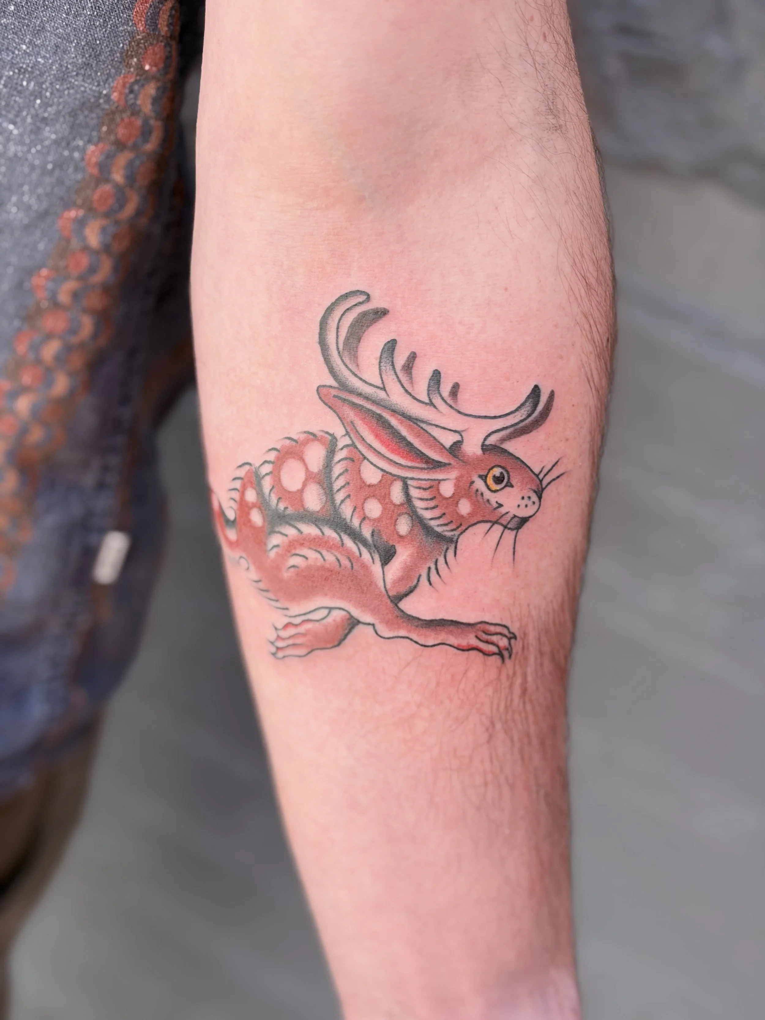 Close-up of a person's arm with a colorful tattoo of a dragon in shades of red, gray, and black.