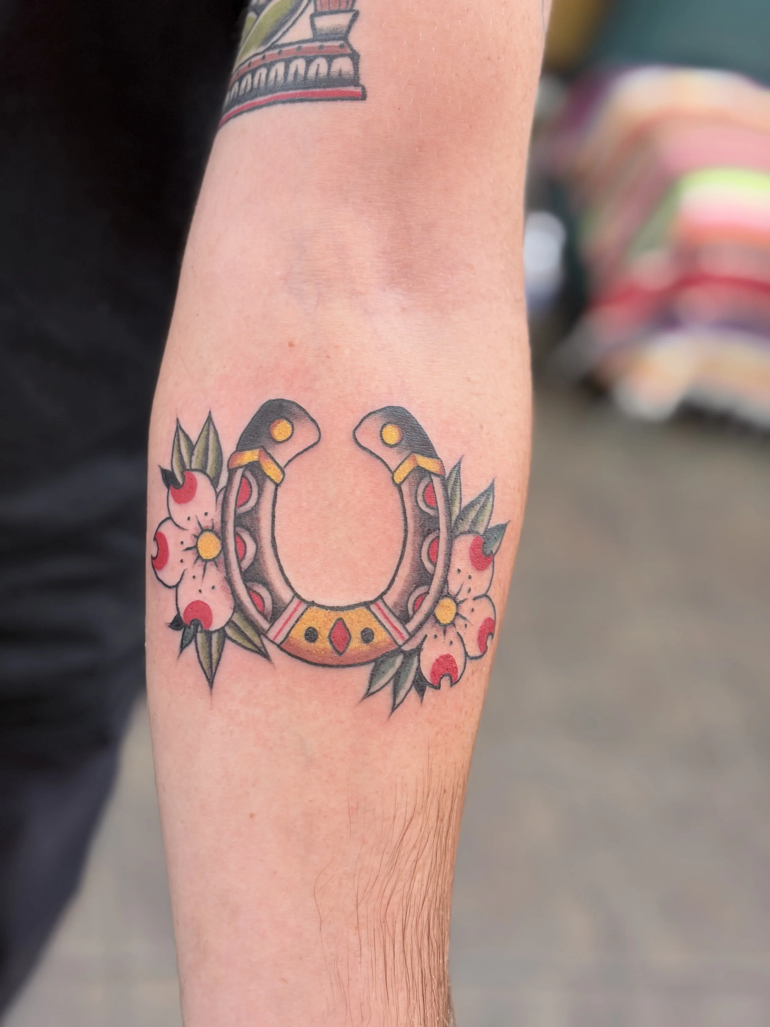A colorful tattoo on a person's forearm featuring a horseshoe with flowers and leaves.