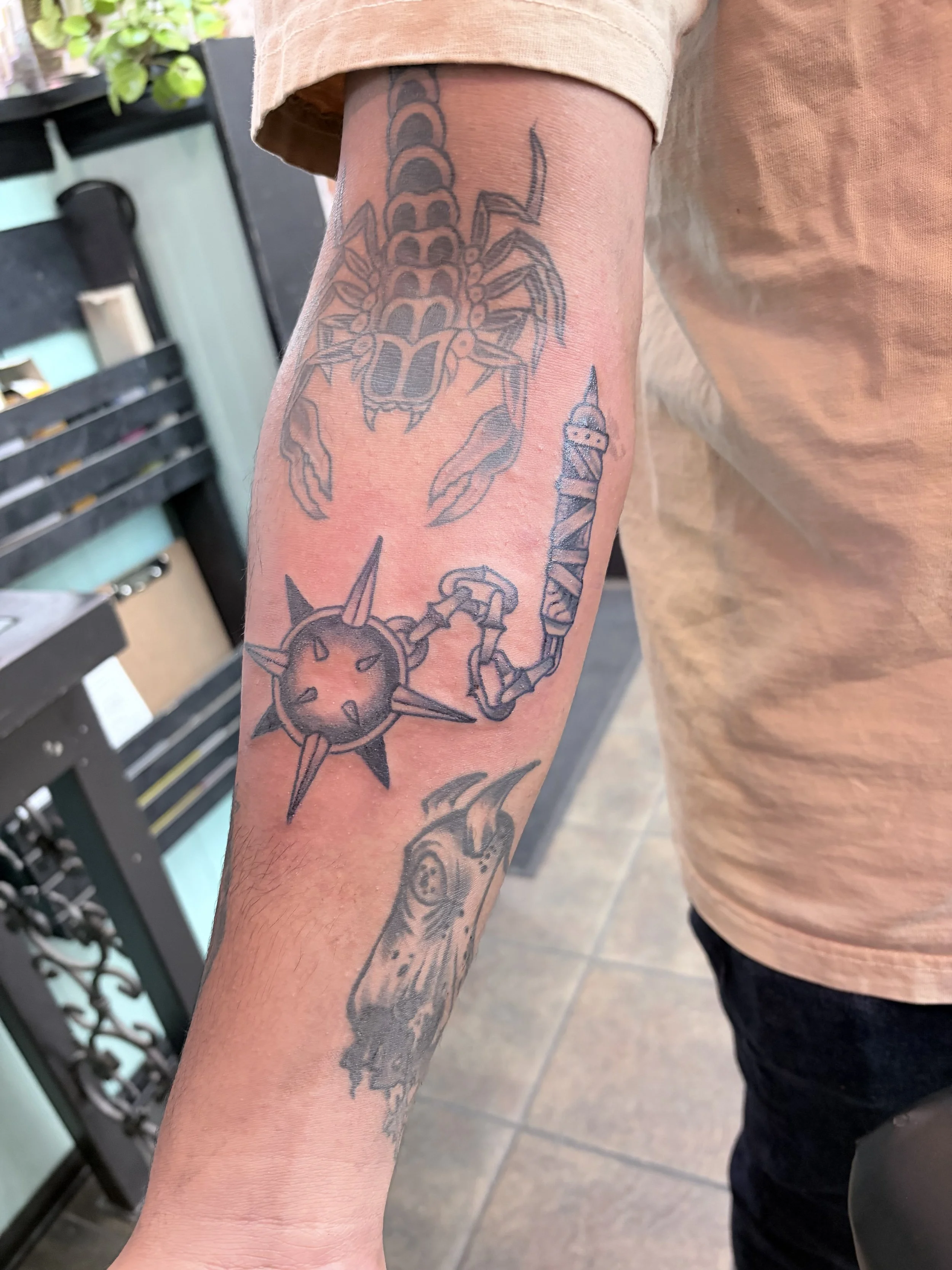 A person's arm with tattoos, including a large scorpion and a shield with spikes, near a black metal rack in an indoor setting.