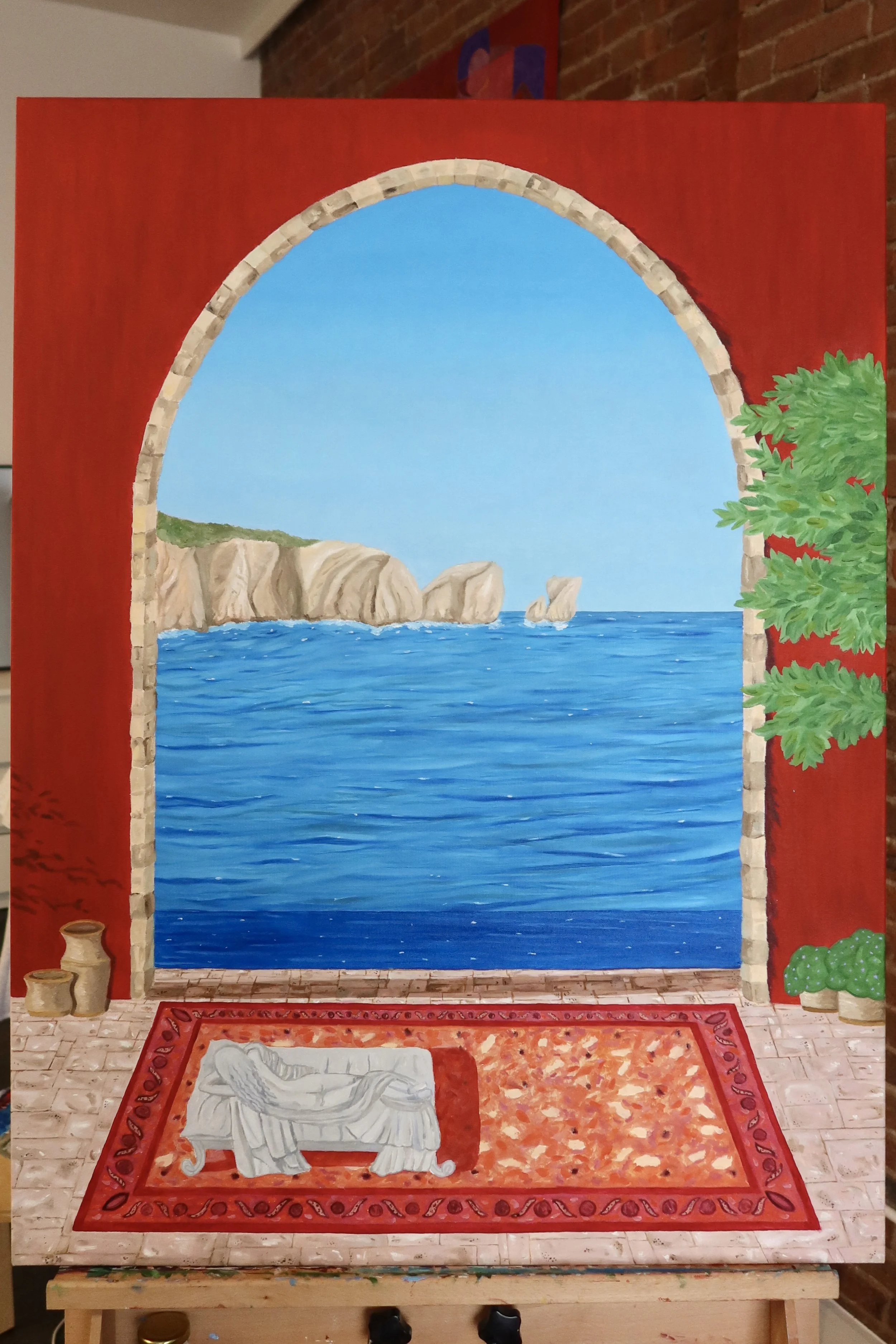 Painting of a seaside landscape seen through an archway with brick borders. The scene includes blue water, rocky formations, green landscape, and a clear sky. The painting is on a red background with greenery on the right side.