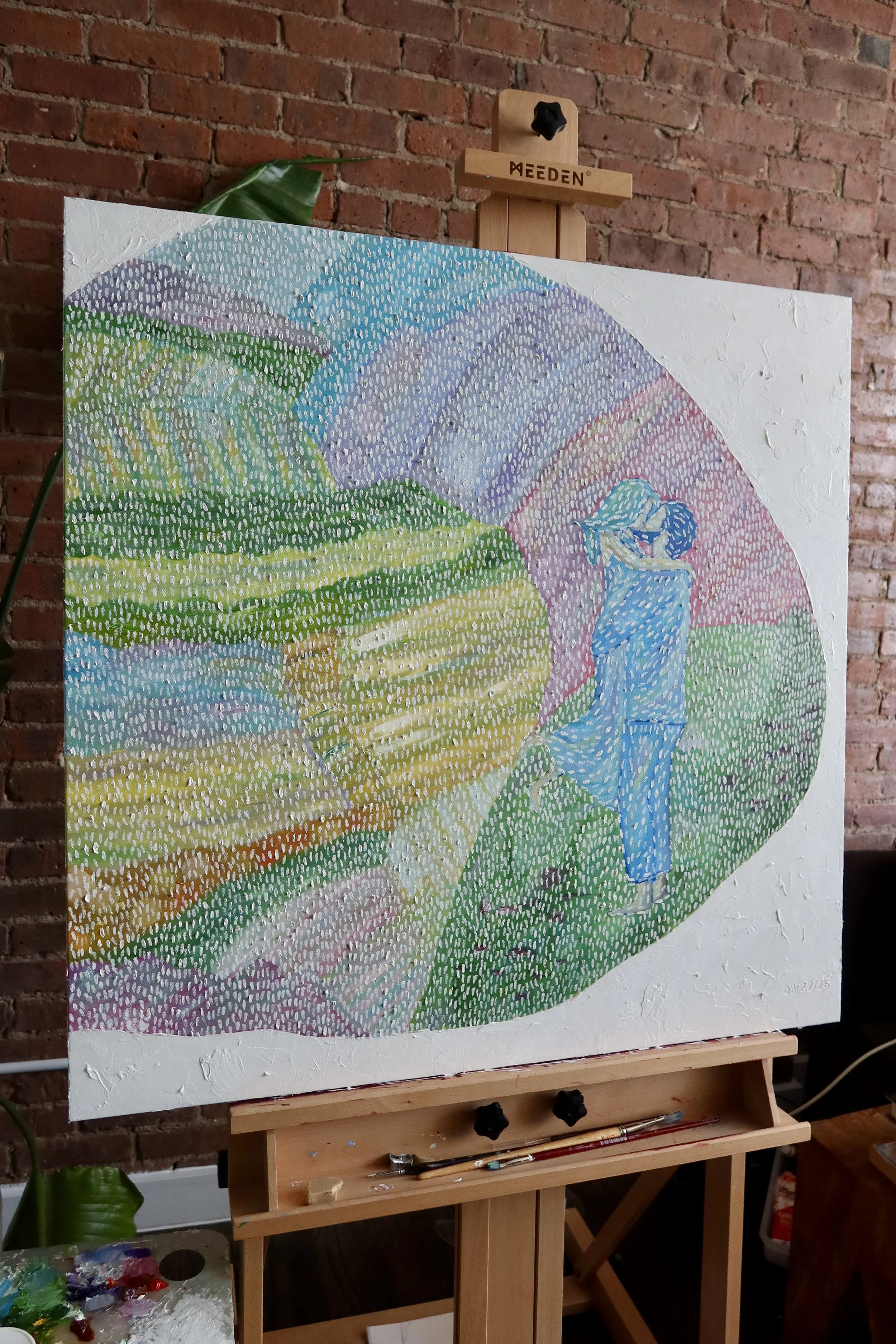 A colorful abstract landscape painting on an easel with a brick wall background. The painting features hills, mountains, and a river in bright colors, created with a dotted or impressionistic style.