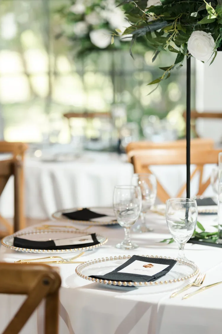 Table setting with clear glassware, black napkins, and decorated plates with pearl-like edges at an elegant event.