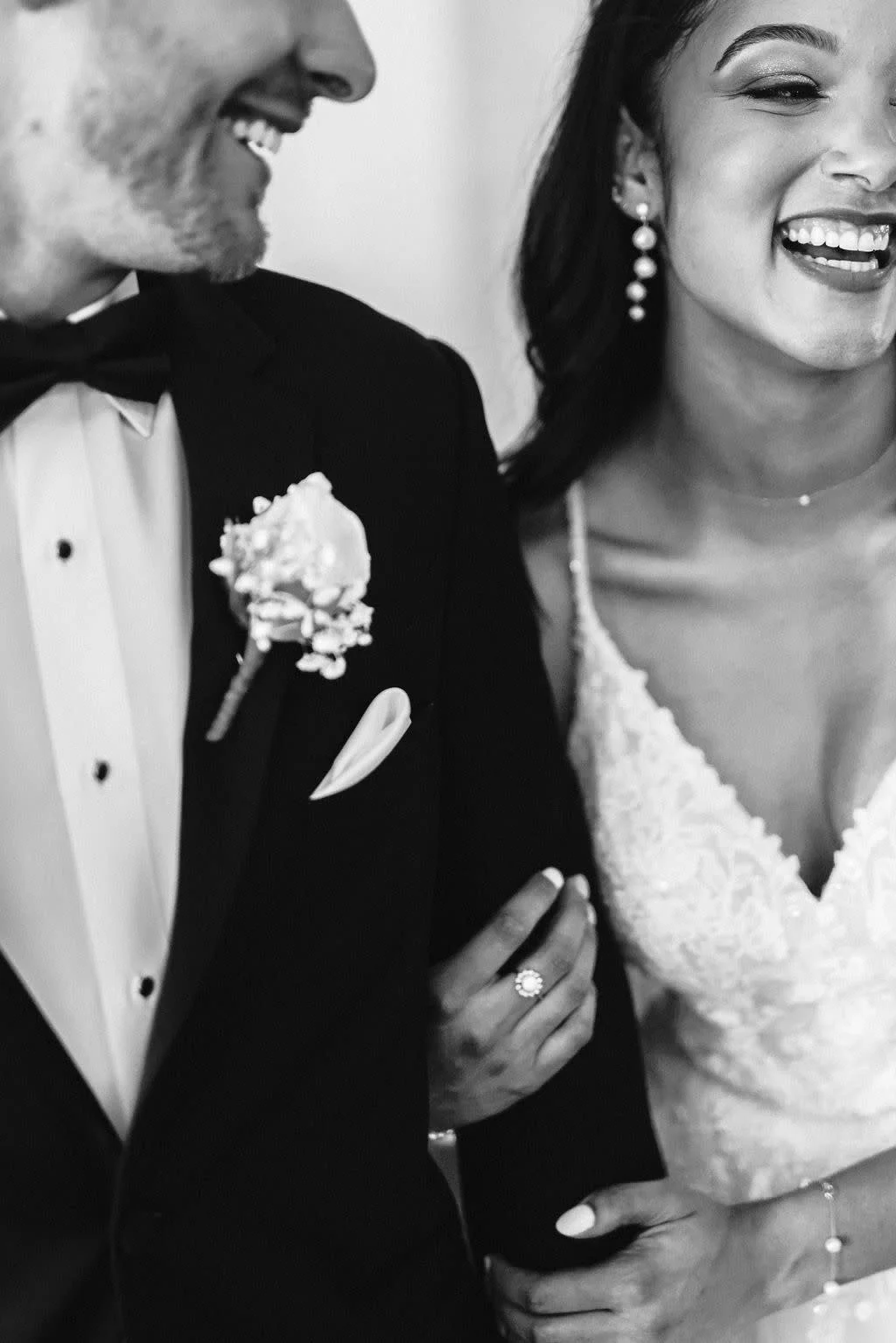 Black and white photo of a smiling bride and groom at their wedding, holding hands, wearing formal wedding attire