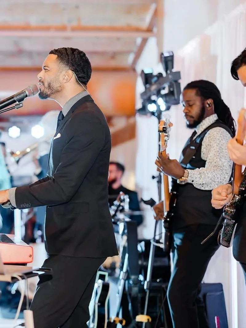 Musicians performing at an indoor event, with a man singing and playing keyboard, and another man playing guitar in the background.