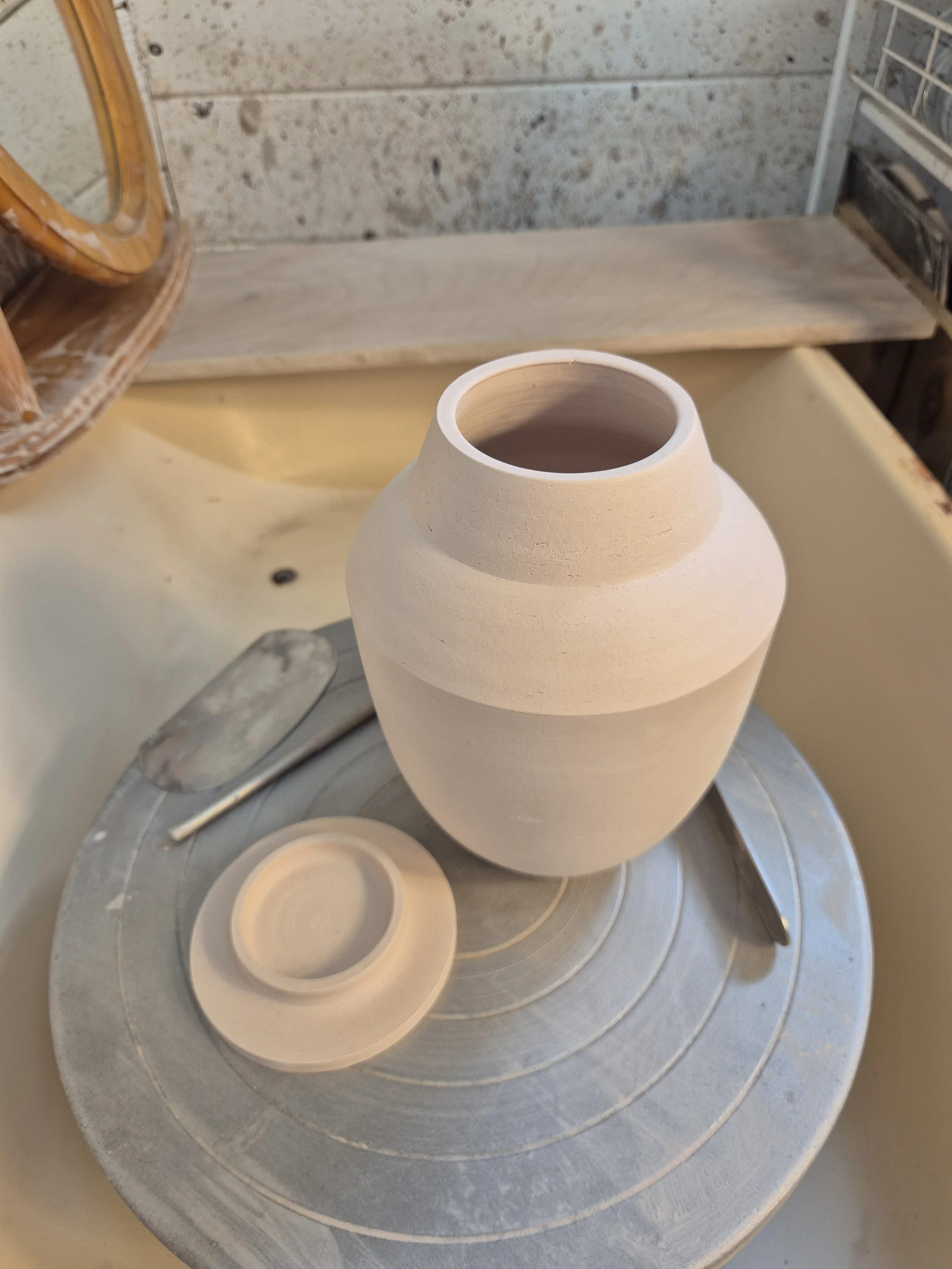 Unfinished ceramic vase on a pottery wheel with clay and tools nearby in a studio setting.