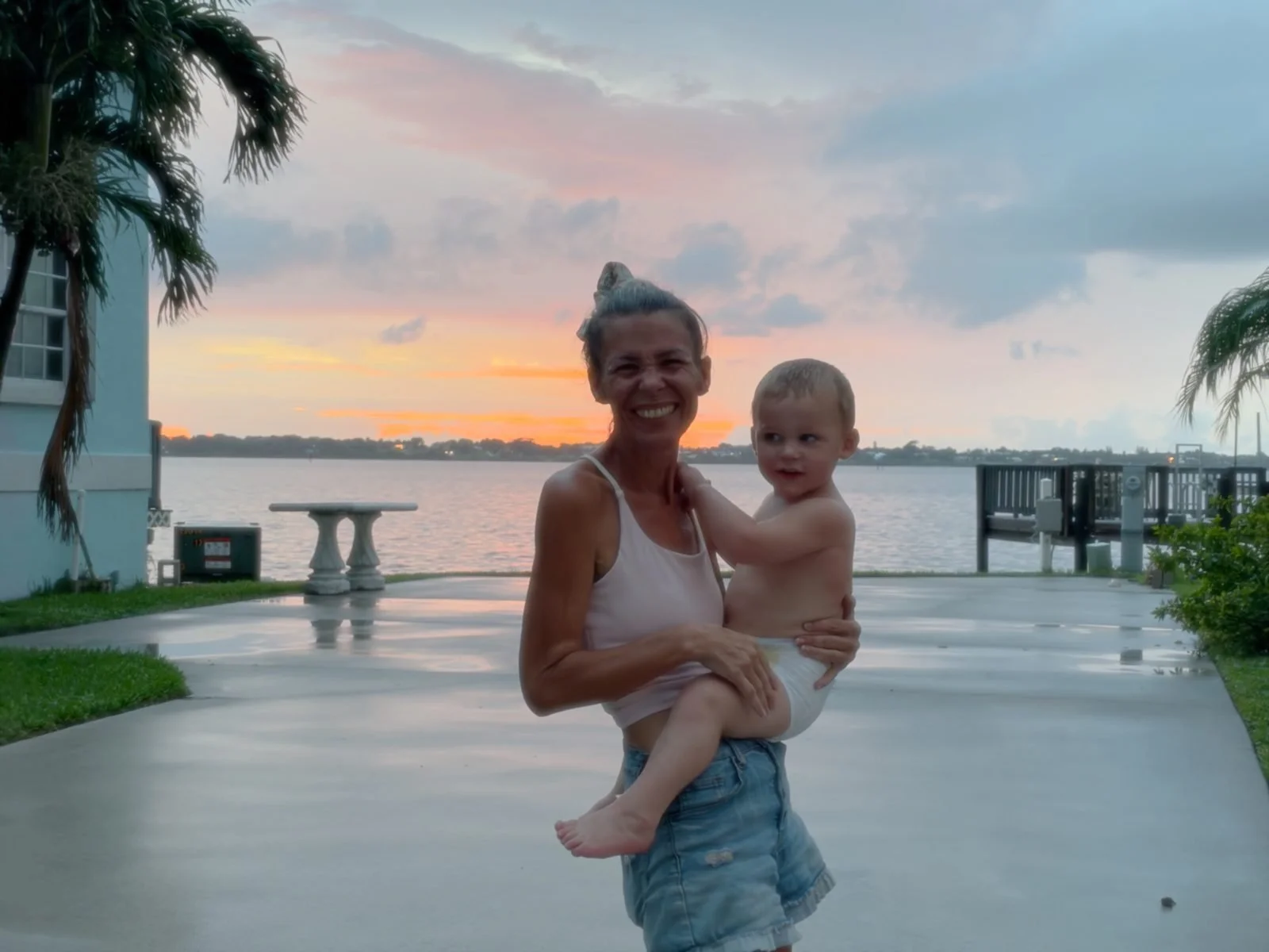 Gigi smiling with Knox on her hip at sunset by the water