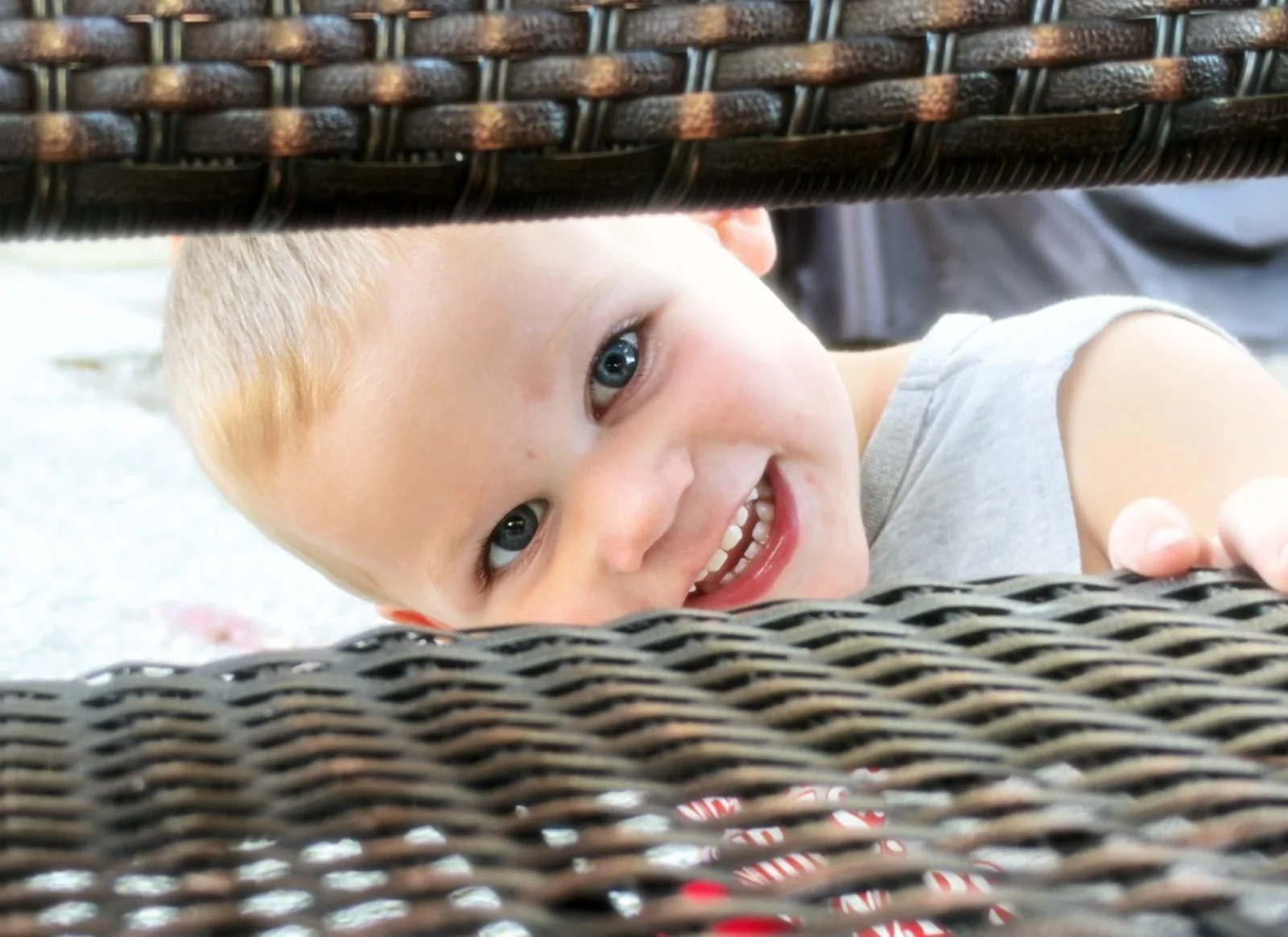 Knox grinning as he peeks through a wicker chair