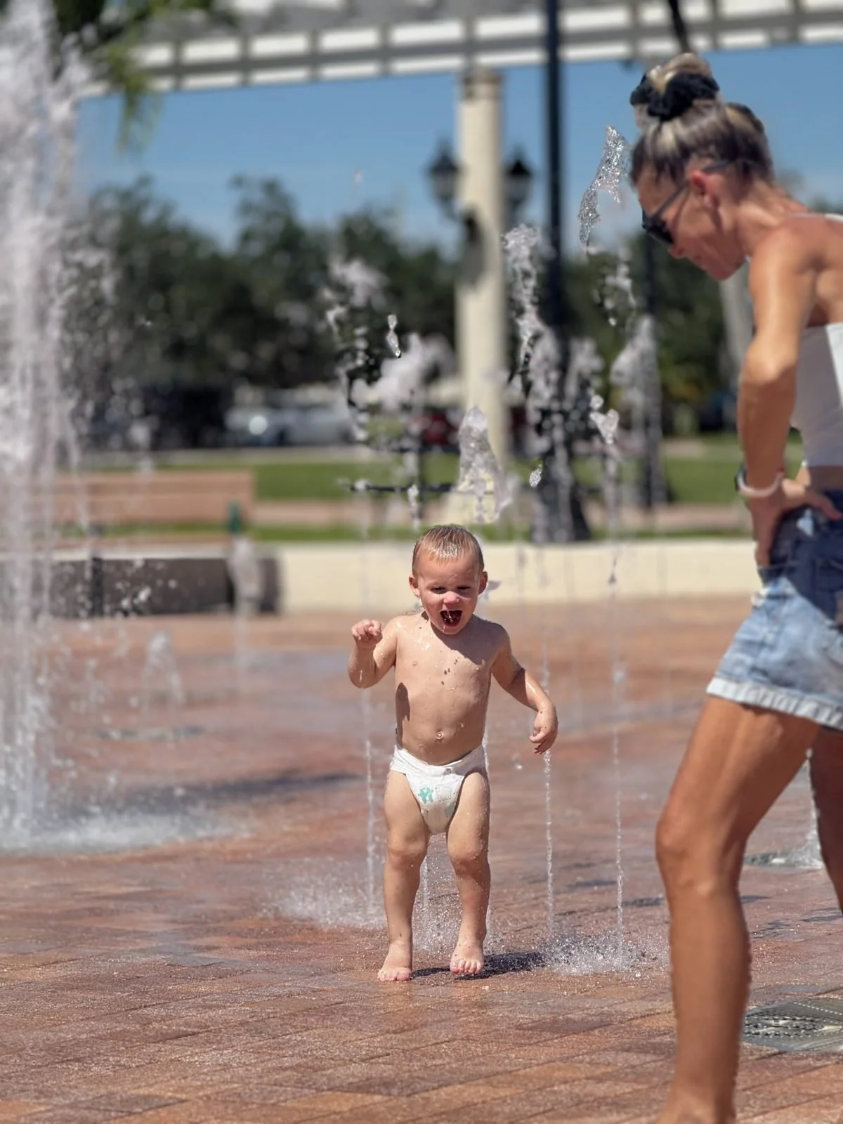 Knox laughing and running through a splash fountain while Gigi watches