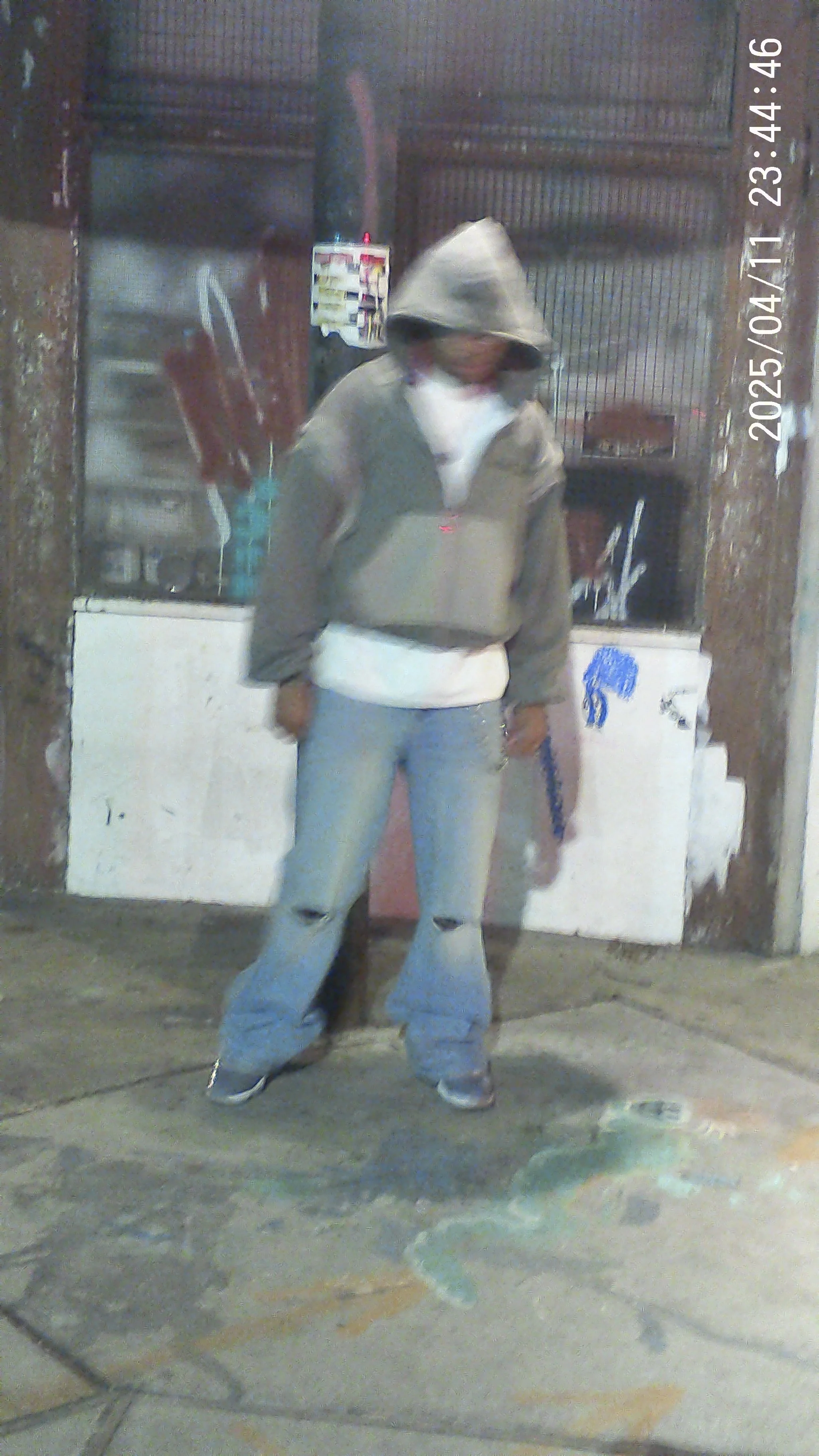 Person wearing a hoodie, white shirt, and ripped jeans standing outside in front of a store with a metal roll-up door.
