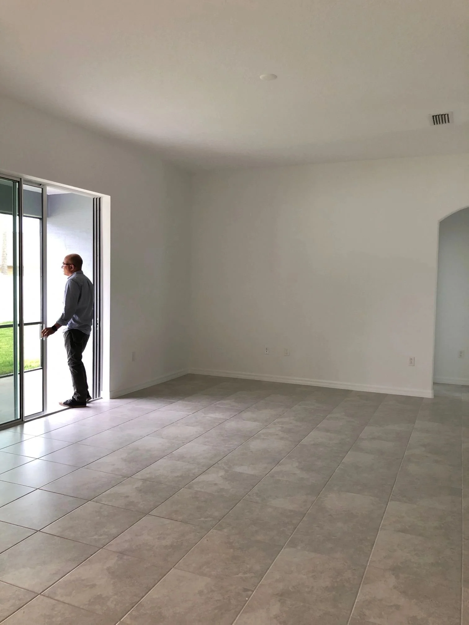 Man standing in an empty room looking outside through sliding glass door.