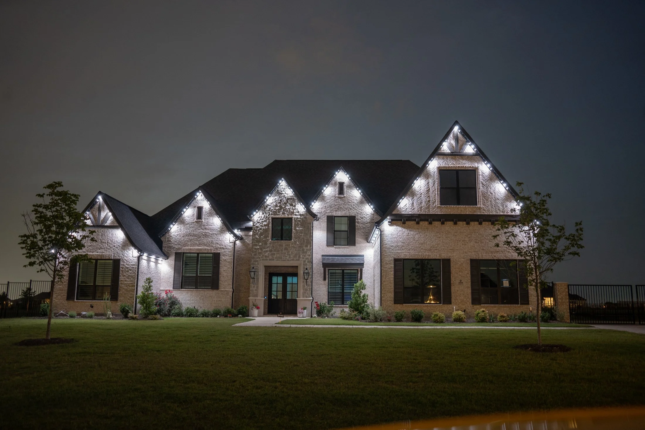 White accent lights illuminate selected points beneath the gables and eaves of a stone home at night.