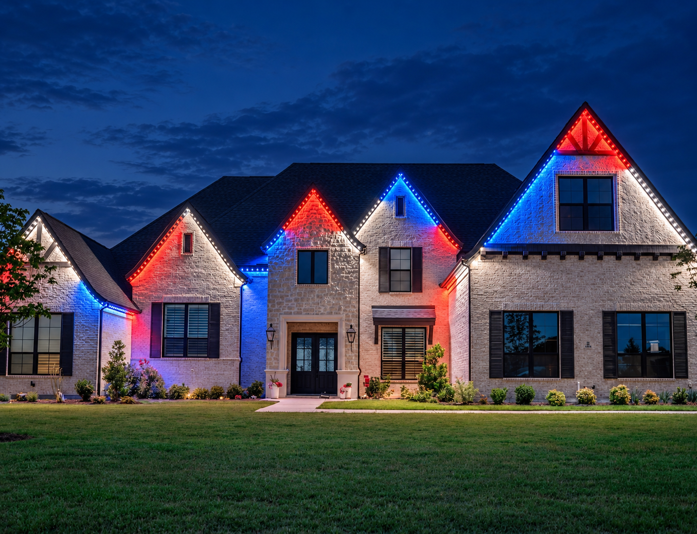 Red, white, and blue permanent lighting outlines a stone home’s gables and front exterior.