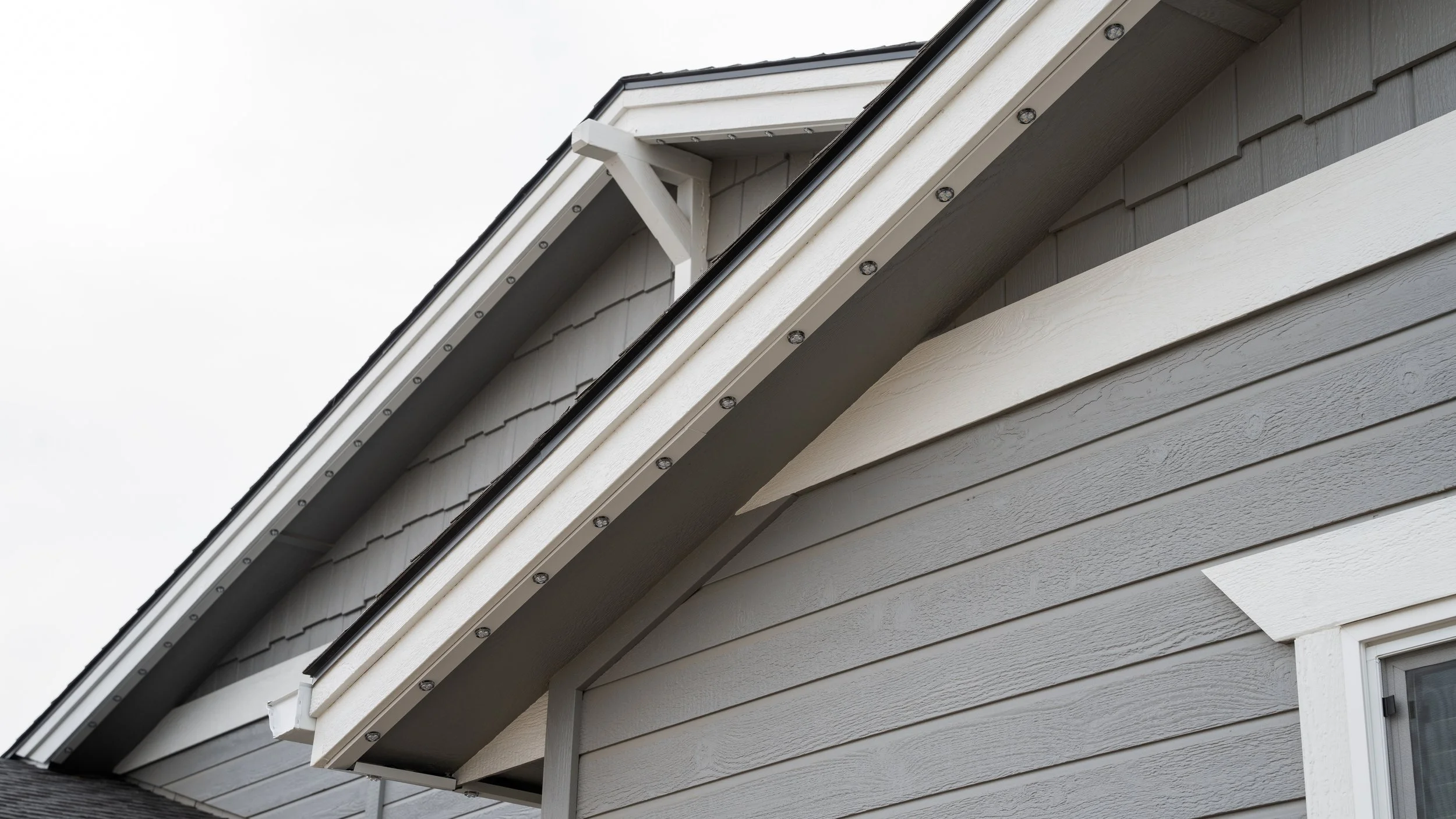 Close-up of permanent lights fitted into a color-matched aluminum channel beneath a gray home’s eaves.