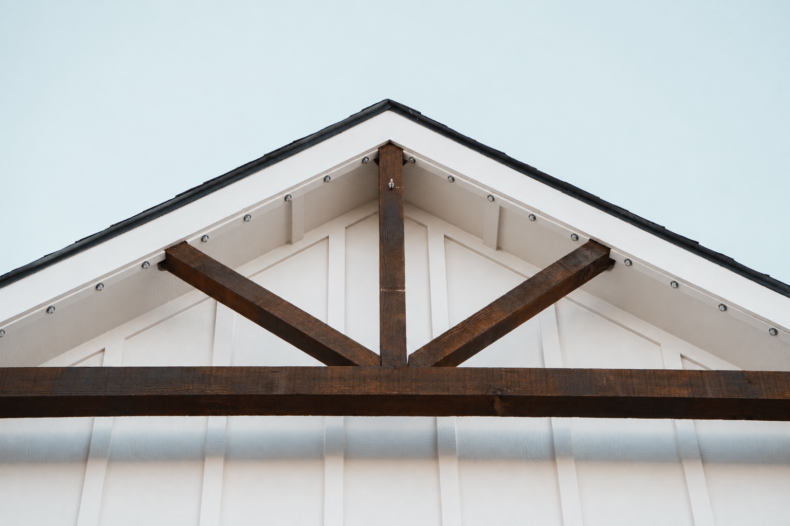 Permanent lighting in a white color-matched channel along a gable with dark timber beams, shown in daylight.