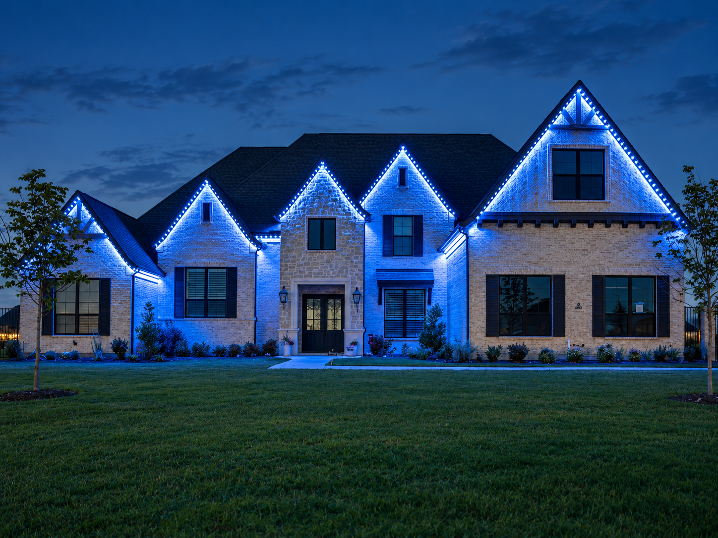Blue permanent lights outline the gables and illuminate the front of a stone home.