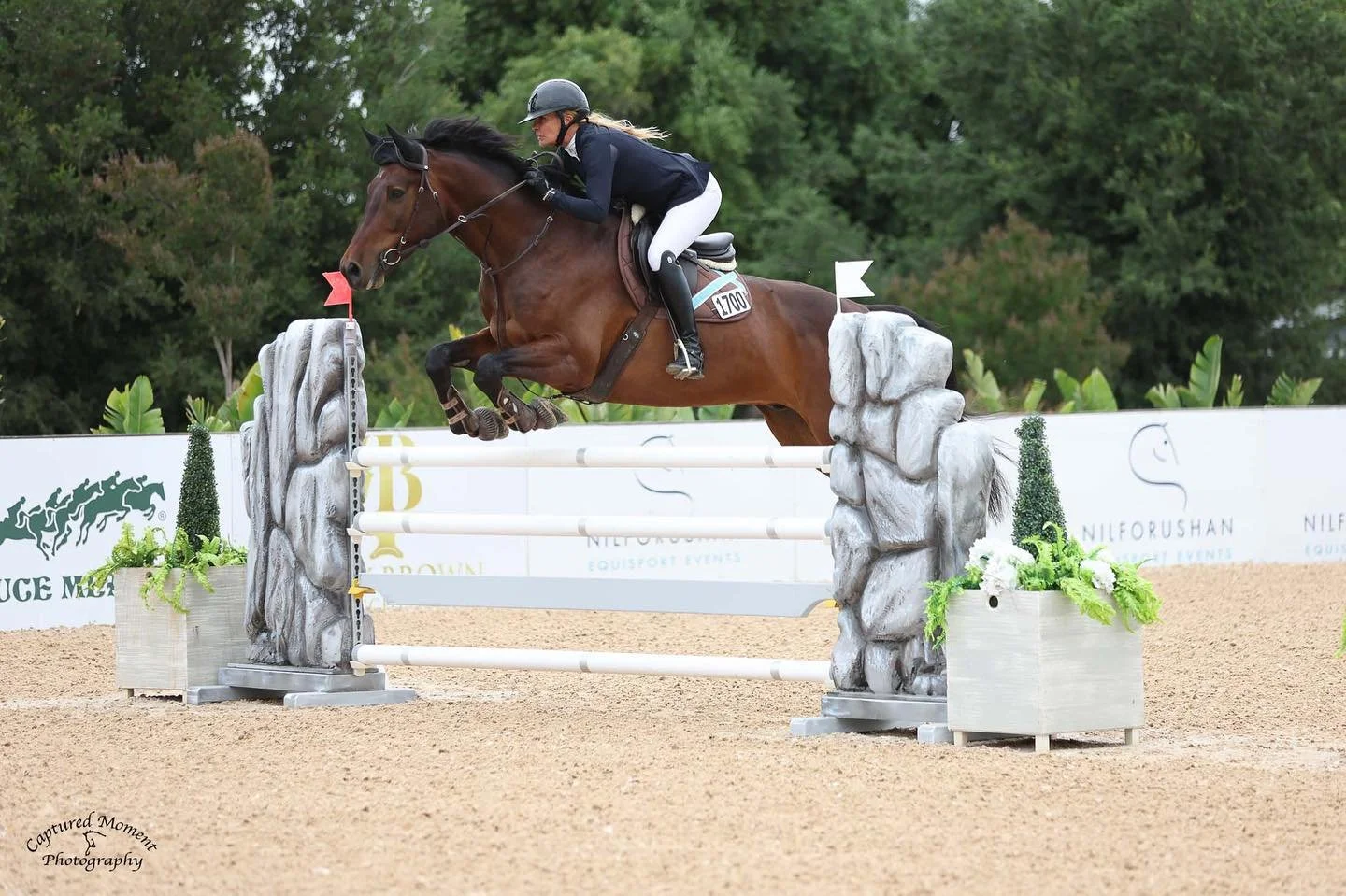 A rider and horse clear a show jumping obstacle resembling rocks and logs during an equestrian event.