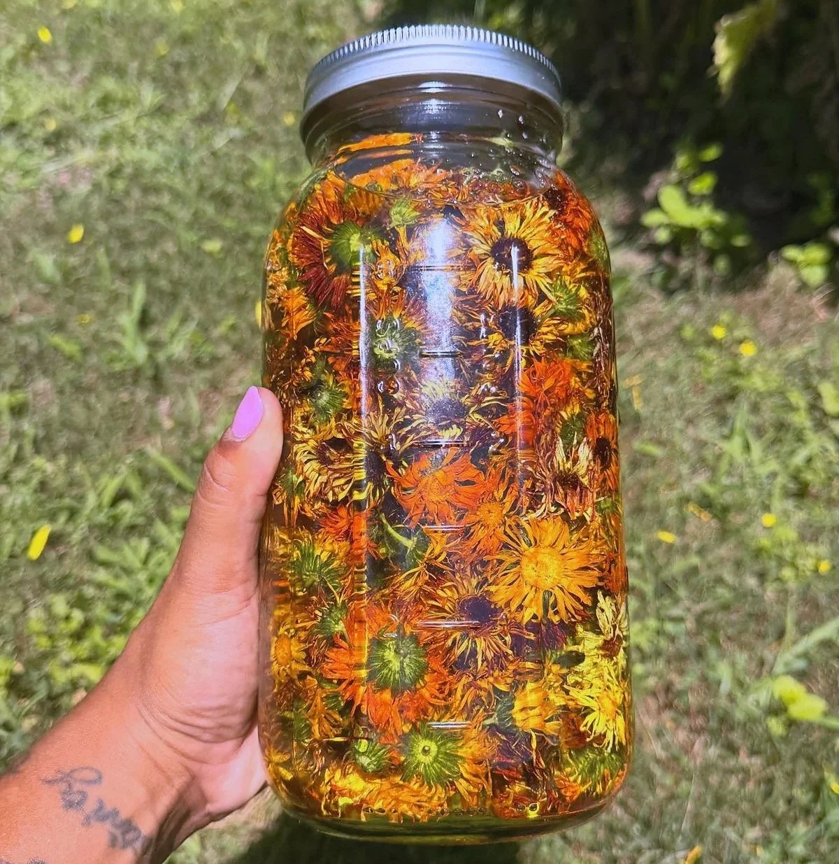 A glass jar filled with colorful dried flowers, with a silver lid, held outdoors on grass.