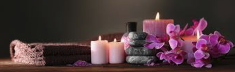 Spa arrangement with rolled towels, lit candles, stacked massage stones, and purple orchids