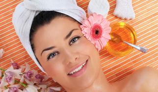 Smiling woman in a towel receiving a spa facial treatment with a pink flower, citrus water, and tropical flowers