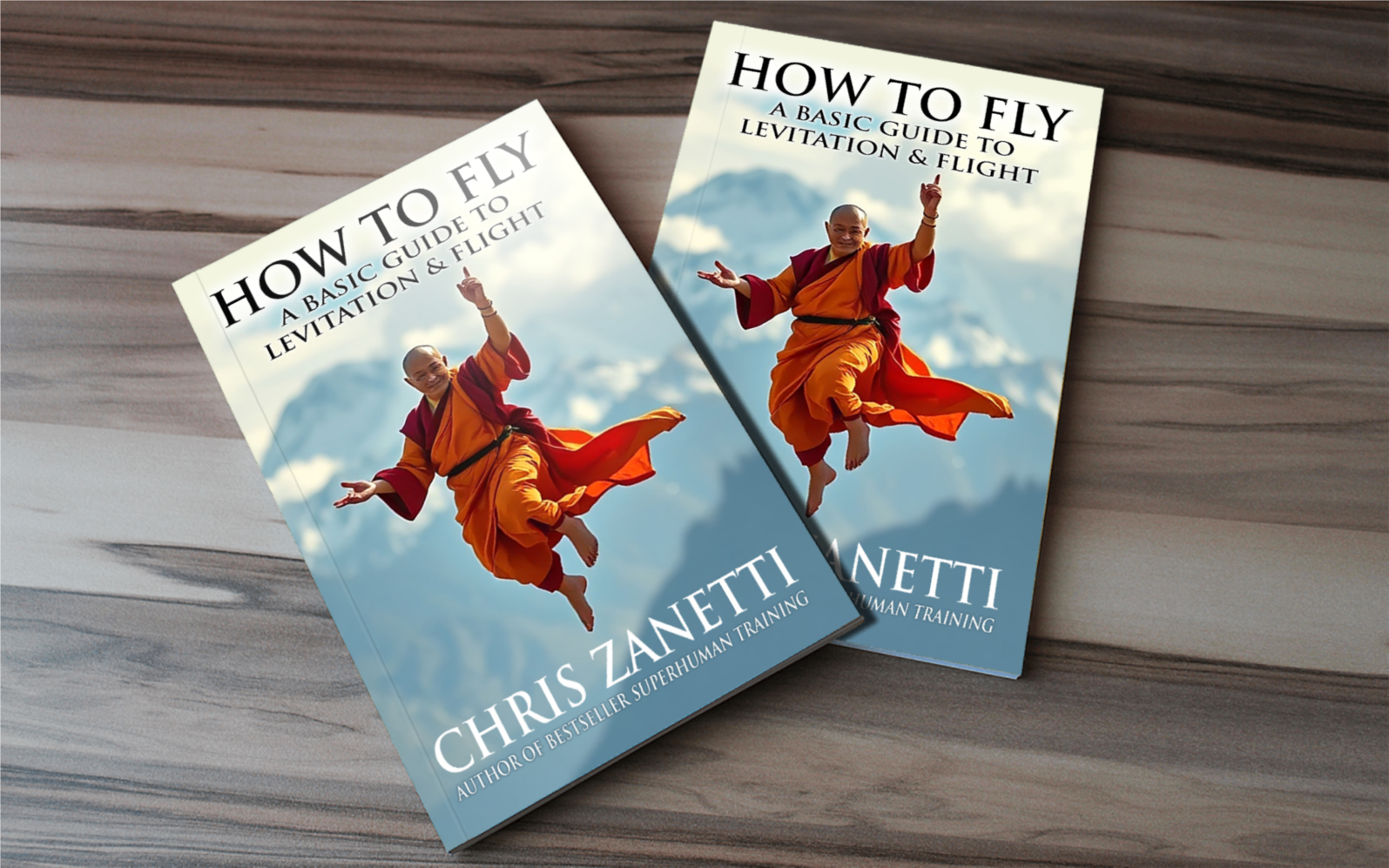 Two copies of a book titled 'How to Fly: A Basic Guide to Levitation & Flight' by Chris Zanetti, featuring a person in orange and red robes flying against a cloudy sky background on the cover, placed on a wooden surface.