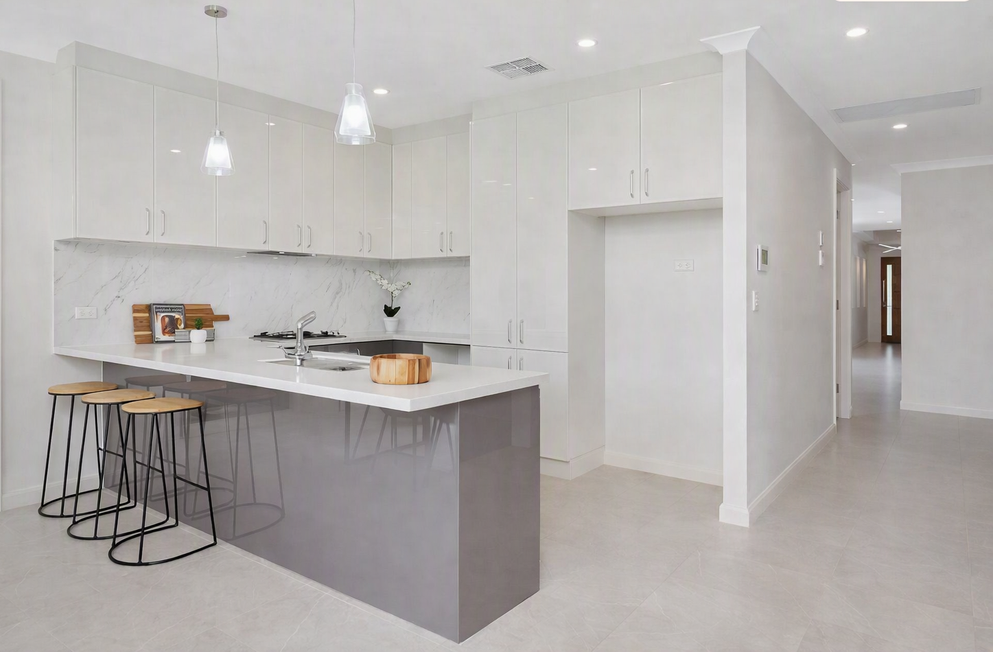Modern white kitchen with marble backsplash, large island, pendant lights, and three bar stools