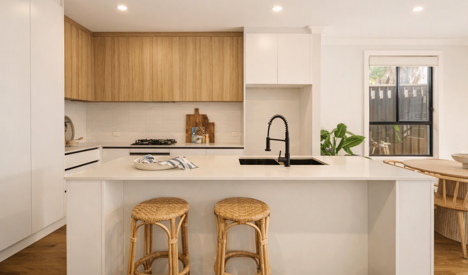 Bright modern white kitchen with wood cabinets, island sink, and two wicker bar stools