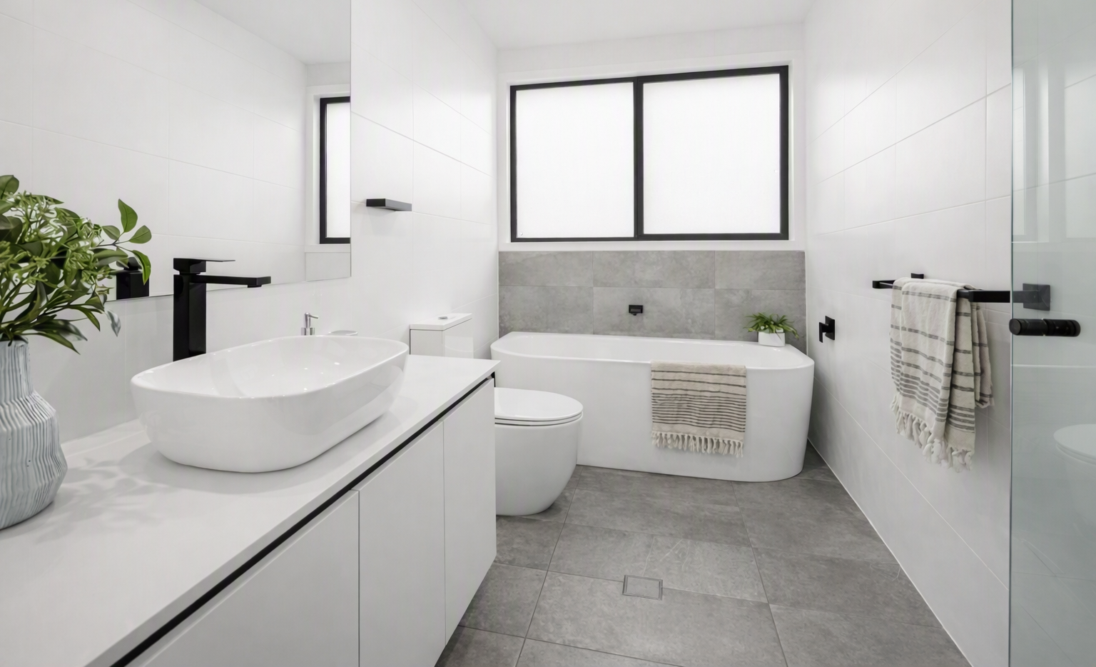 Modern white bathroom with freestanding bathtub, vessel sink vanity, toilet, gray tile floor, black fixtures, and striped towels