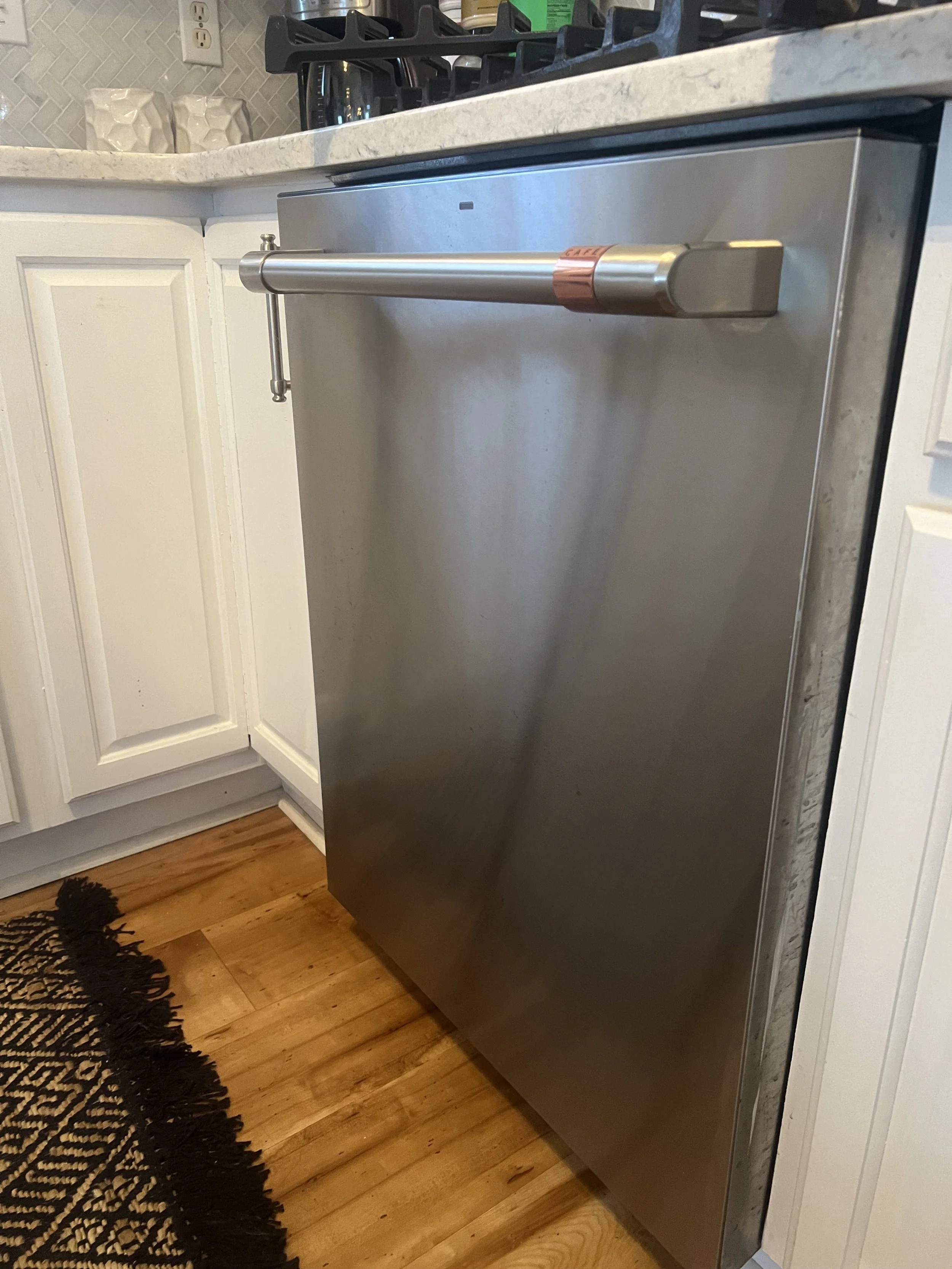 Stainless steel dishwasher installed under a kitchen counter next to white cabinet doors on a wood floor.